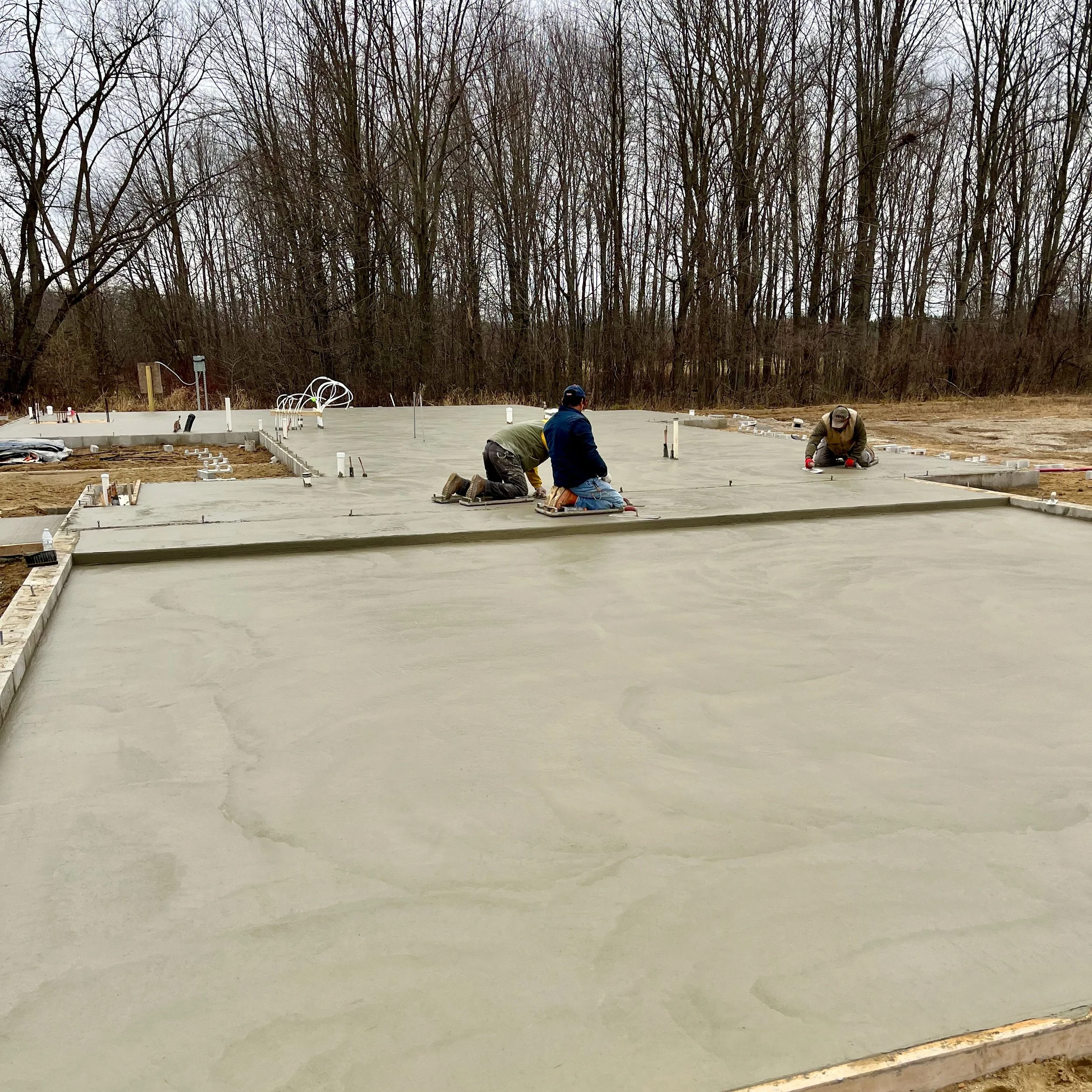 Two men work to finish a concrete slab for a new house.