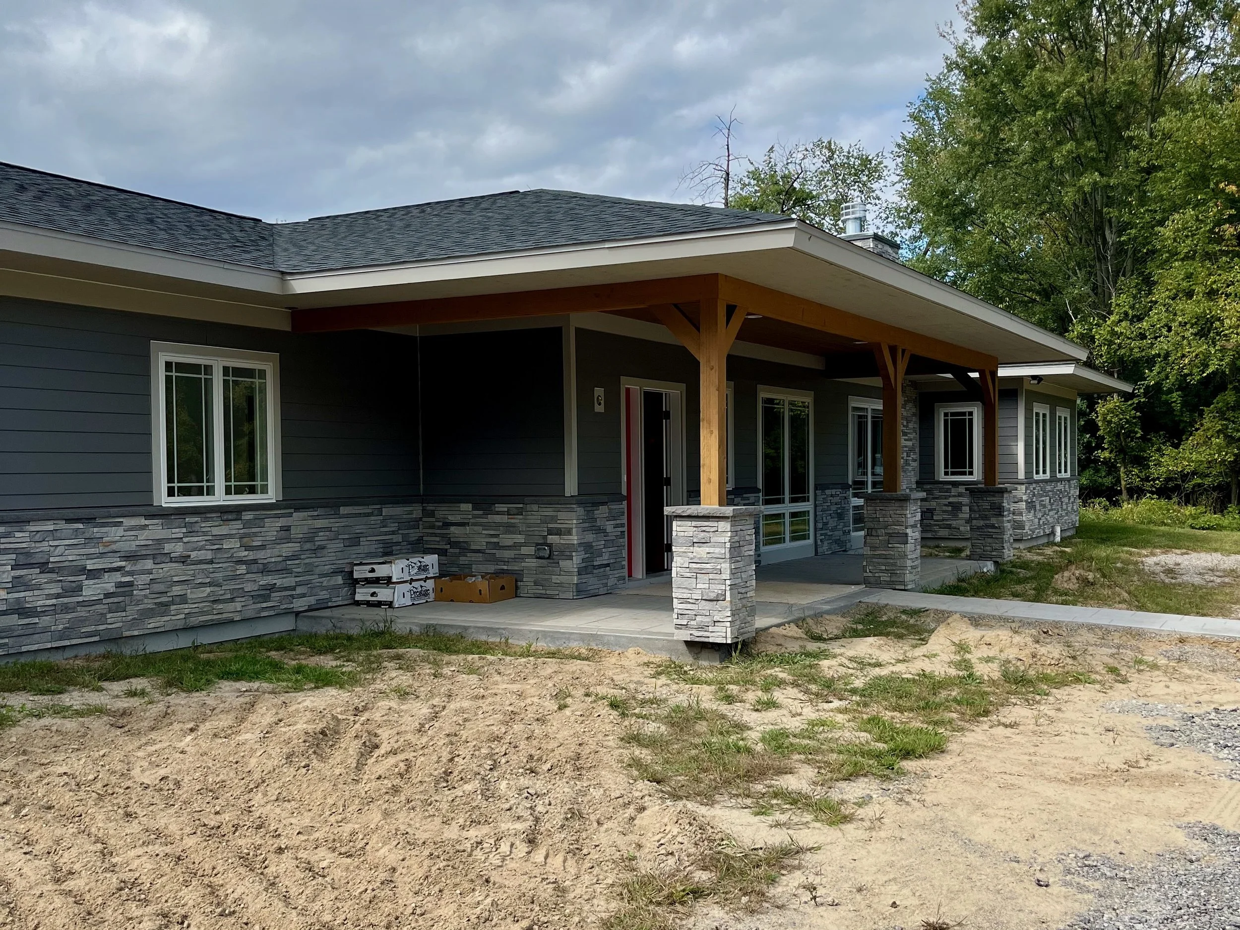 View of finished exterior of house with blue gray siding and gray field stone half wall from the ground to the bottom of windows.