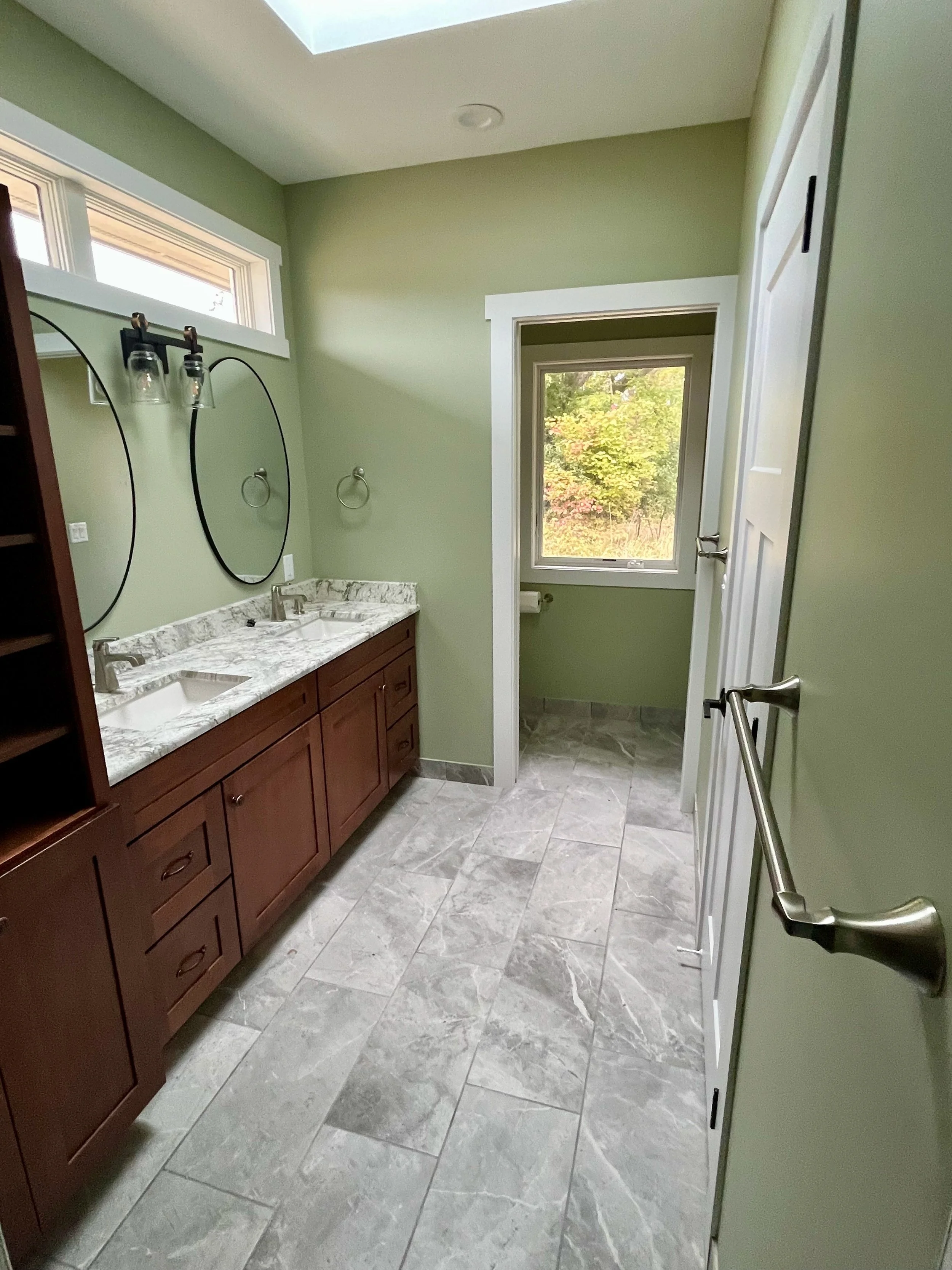 Finished bathroom with tile floor, sage green painted walls and fine wood vanities. There is a separate toilet room at back of the bathroom.