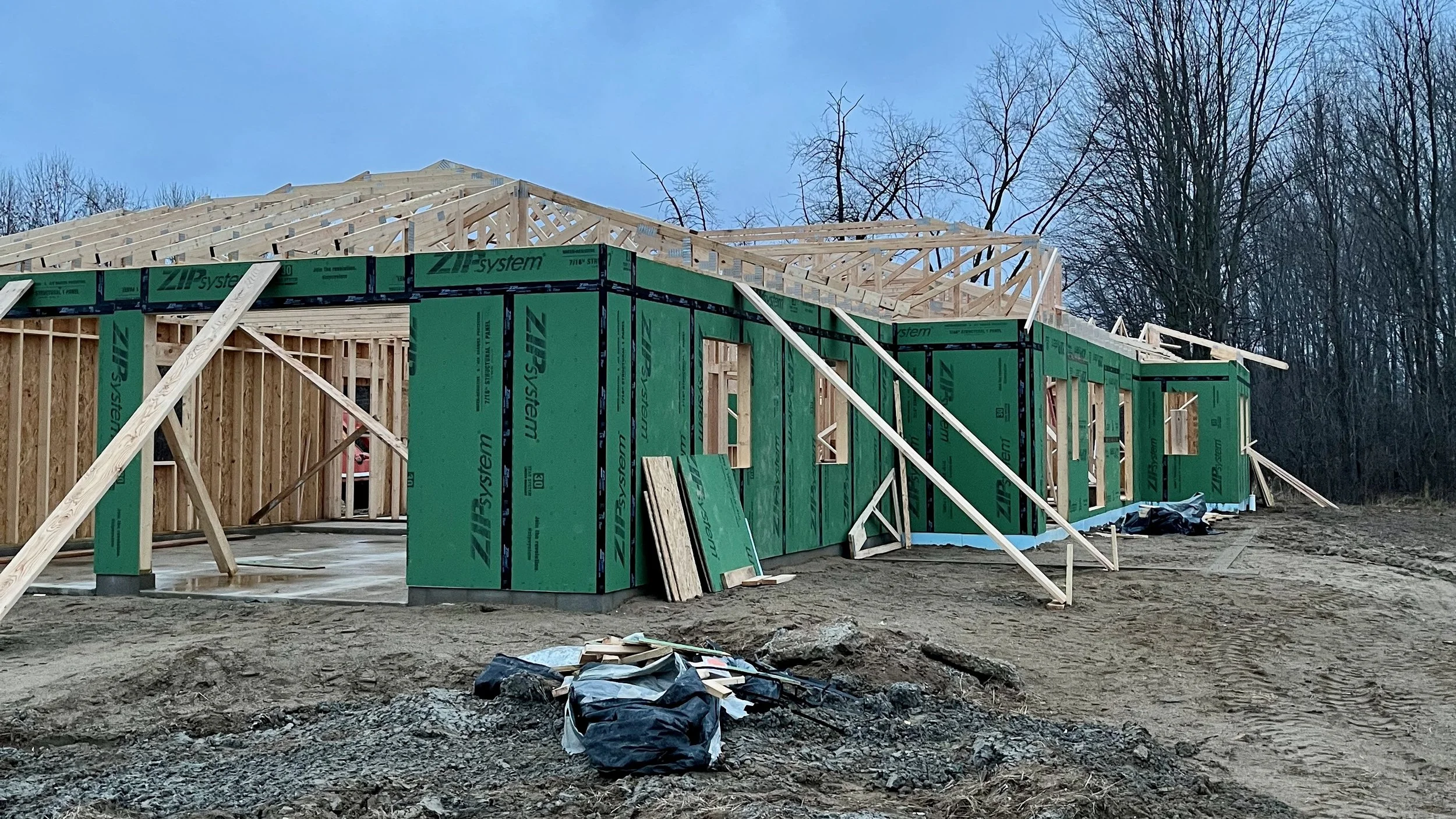 Wide view of a home under construction with green ZIP Wall sheathing on the walls and exposed wood trusses on the roof.