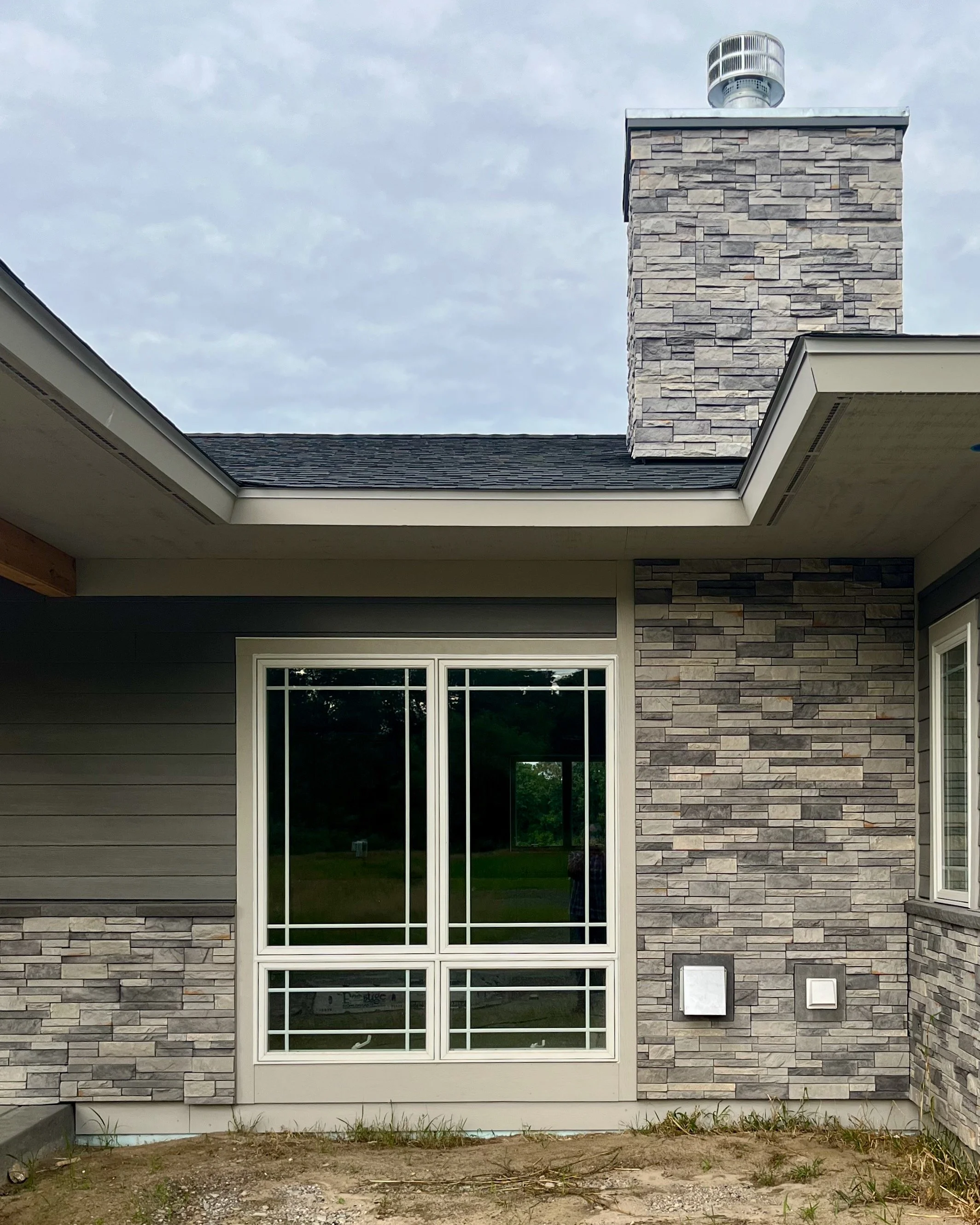 Exterior view of gray fieldstone chimney and window.