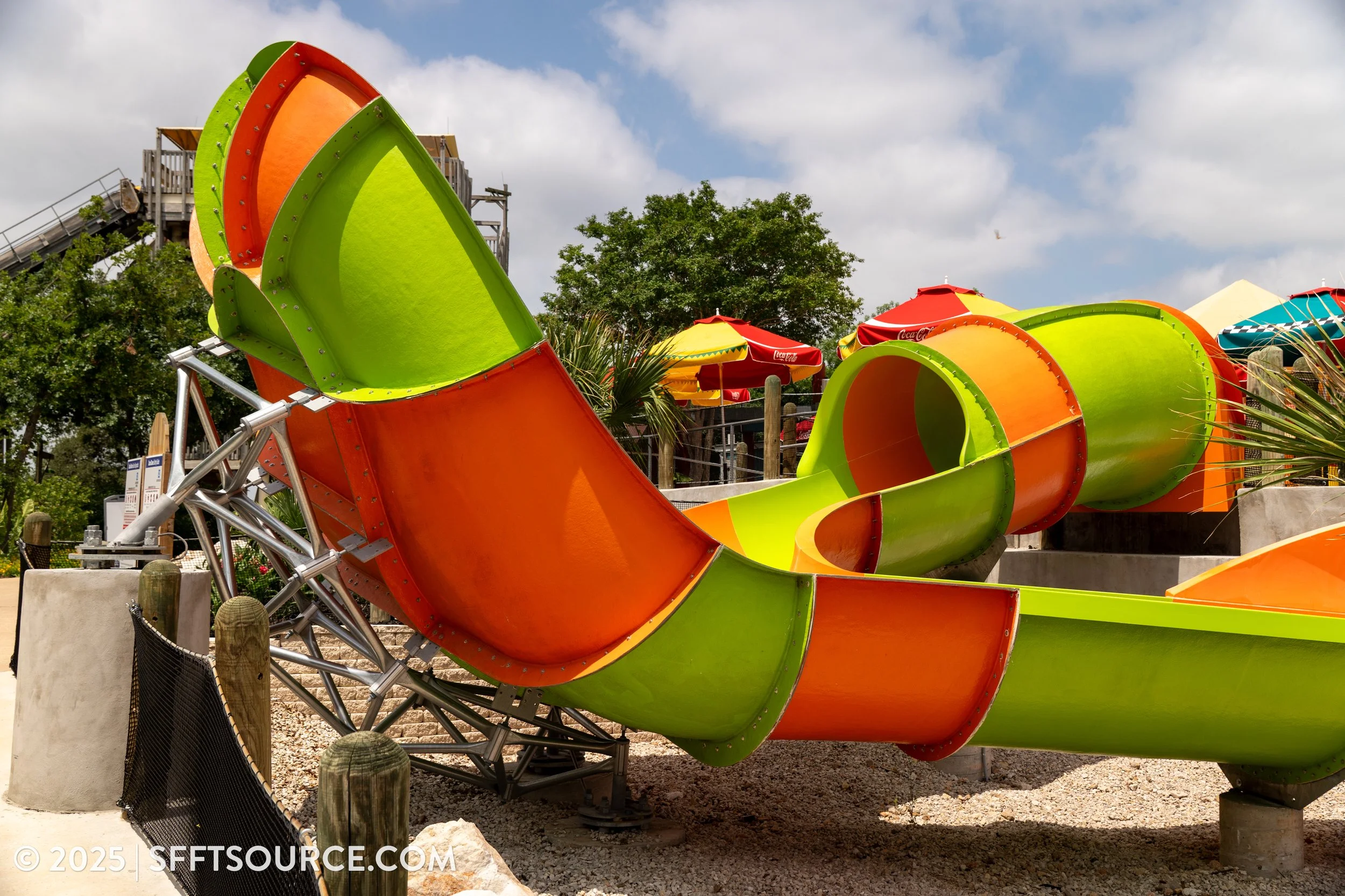 Colorful outdoor playground slide with orange, green, and yellow sections under a partly cloudy sky.