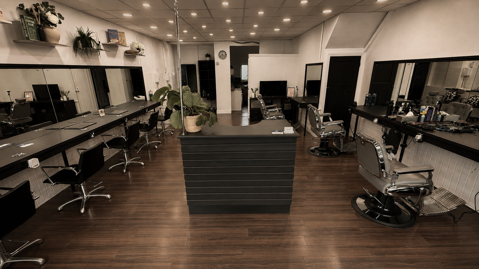 Empty hair salon with styling stations, mirrors, chairs, and a front reception desk in the center, decorated with books, plants, and flowers.