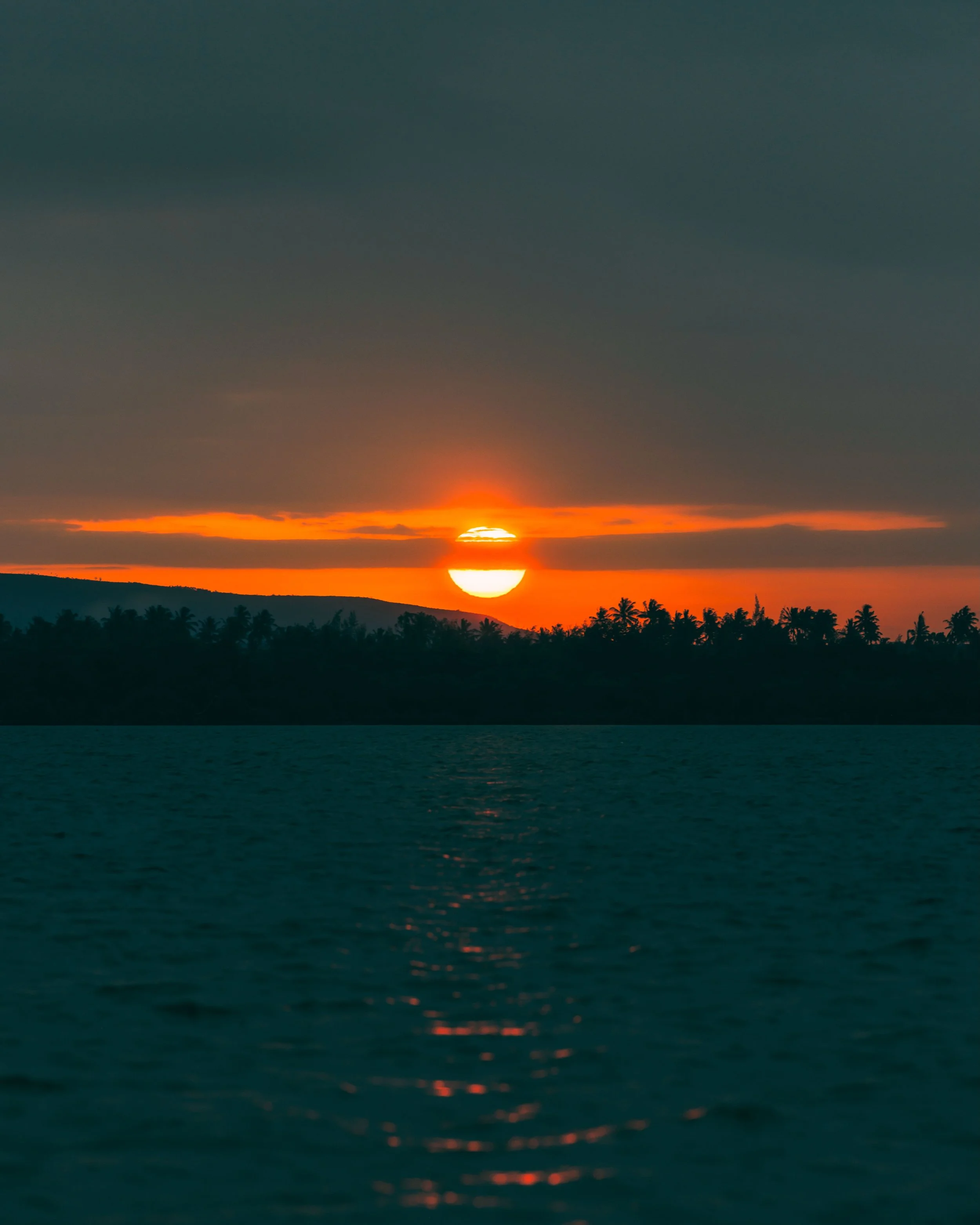 The final act at Mida Creek.

There&rsquo;s a profound contrast when the sky burns this intense, fiery orange against the deep, heavy teal of the water. Watching the sun cut through the clouds and finally sink behind the distant treeline feels less l