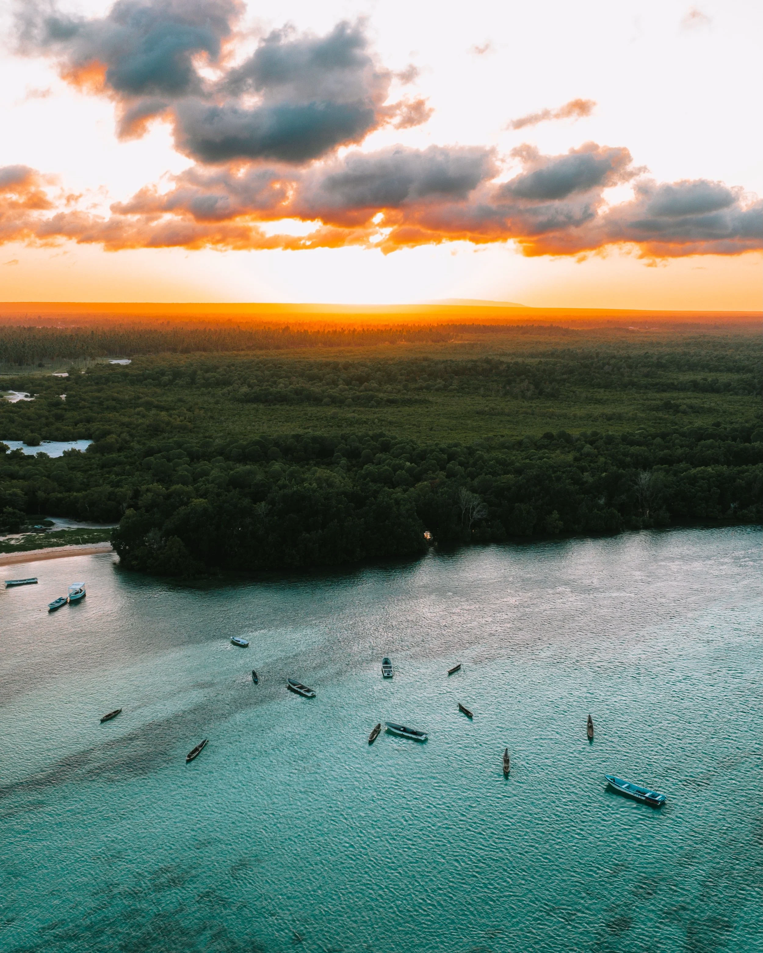 Where the Tide Keeps Time

The sun drops behind the mangrove belt and the creek turns copper, the last boats resting on still water. From above, the fleet scatters across pale jade shallows &mdash; dugouts and skiffs anchored where the seagrass runs 