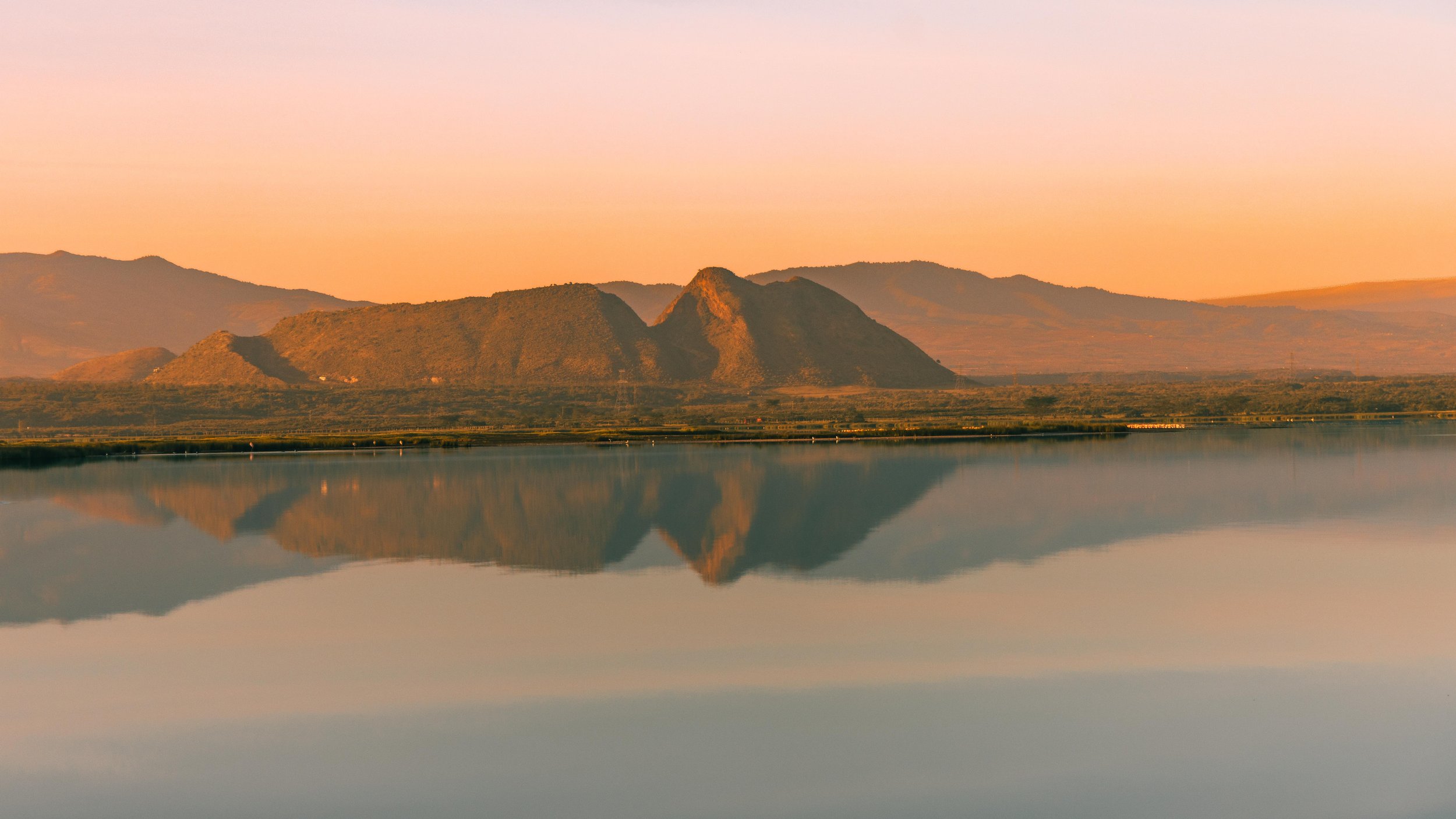 A scenic landscape with a mountain range reflected in a calm body of water during sunset.