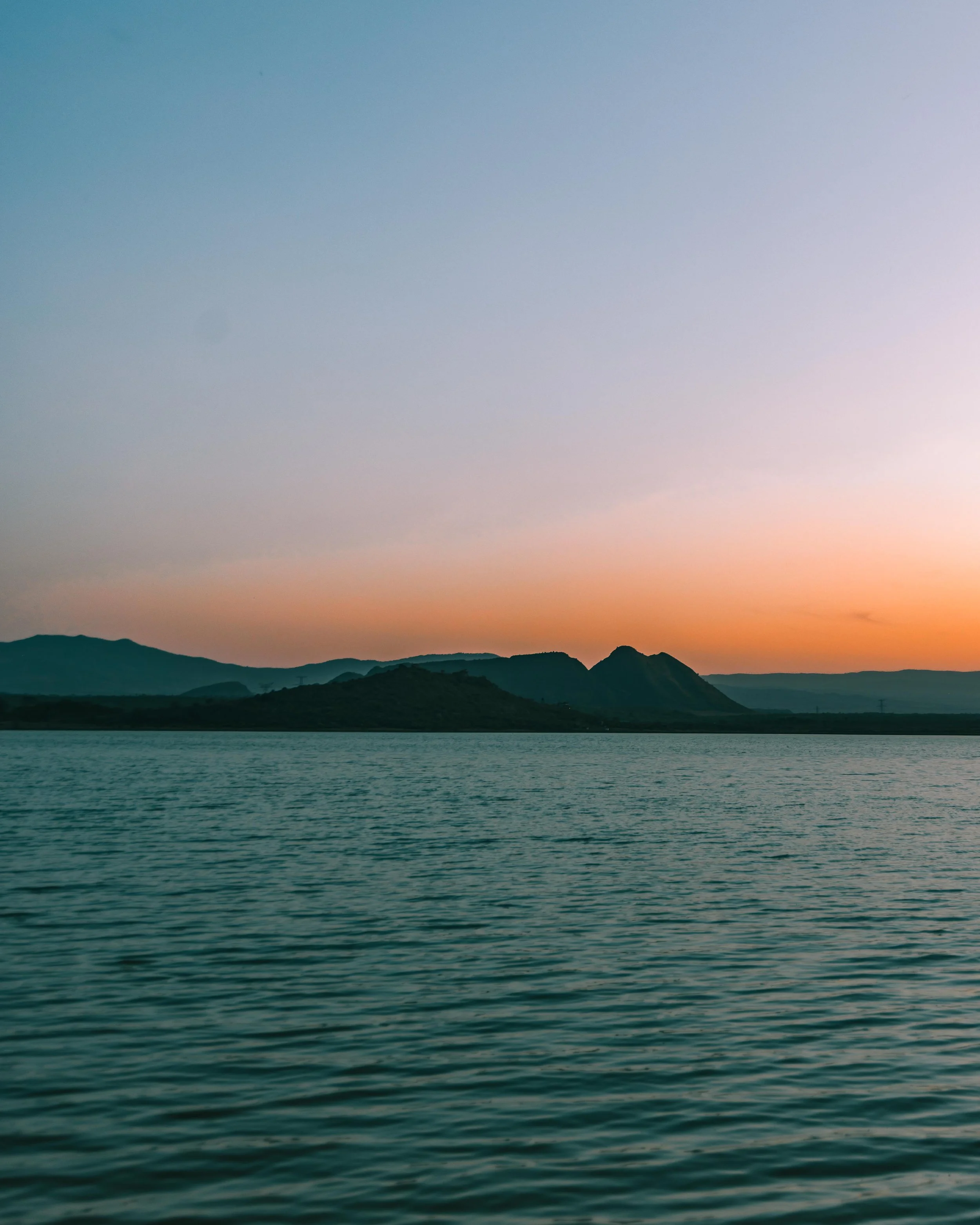 A tranquil lake with dark silhouettes of mountains in the background and a soft gradient sky at sunset.
