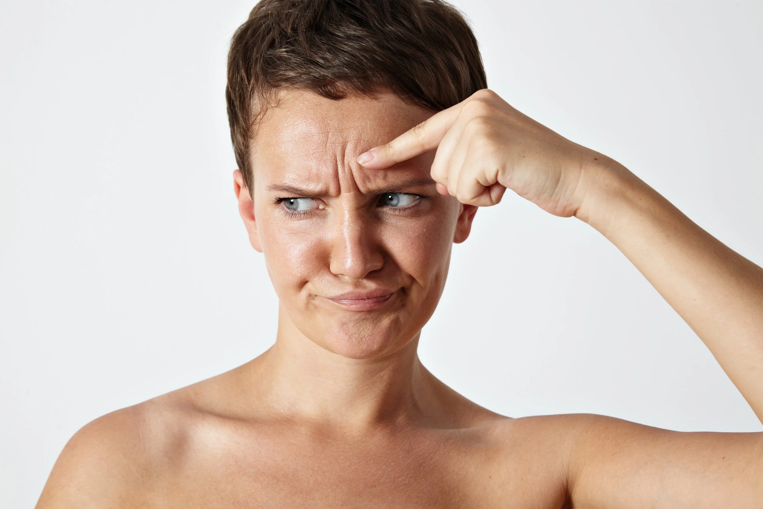 Eine junge Frau mit kurzen braunen Haaren macht nachdenklich eine Grimasse, während sie die Stirn mit dem Finger zwickt.