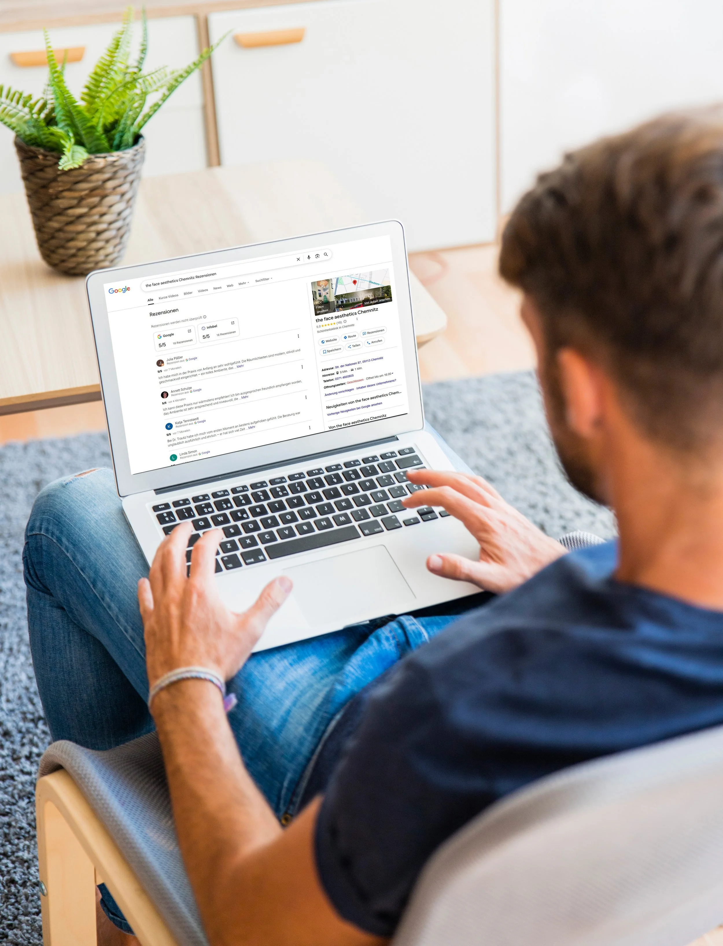 Ein Mann sitzt auf einem Stuhl und nutzt einen Laptop, auf dessen Bildschirm eine Google-Rezensionsseite zu 'the face ästhetics Chemnitz' sichtbar ist. Im Hintergrund befindet sich eine Pflanze in einem Korb.