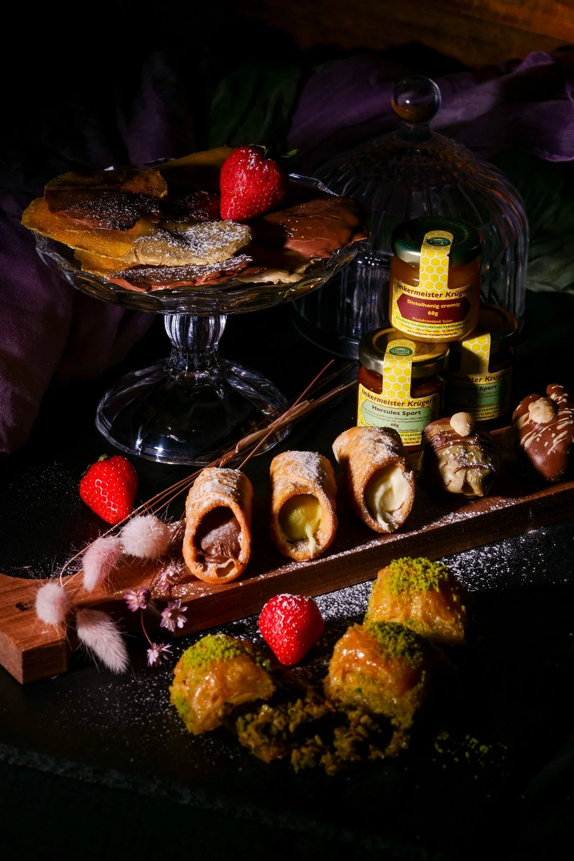 Verschiedene Süßigkeiten und Honig, darunter Eiswaffeln mit Schokolade, Fruchtgummis, Honigtöpfe und mit Pistazien bedeckte Süßigkeiten, auf einem dunklen Hintergrund.
