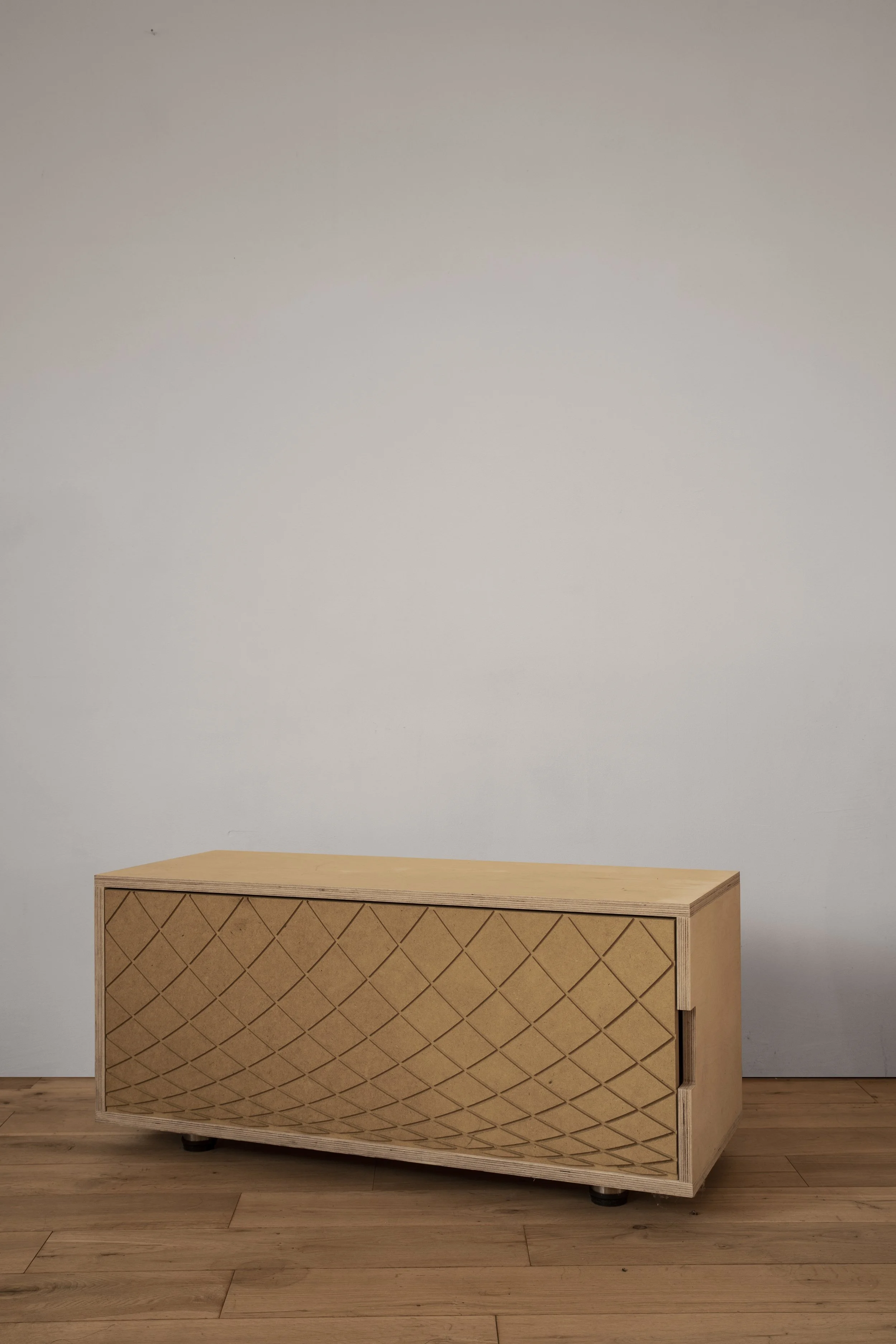 A wooden cabinet with a diamond pattern on the sliding door, placed on a hardwood floor against a plain white wall.