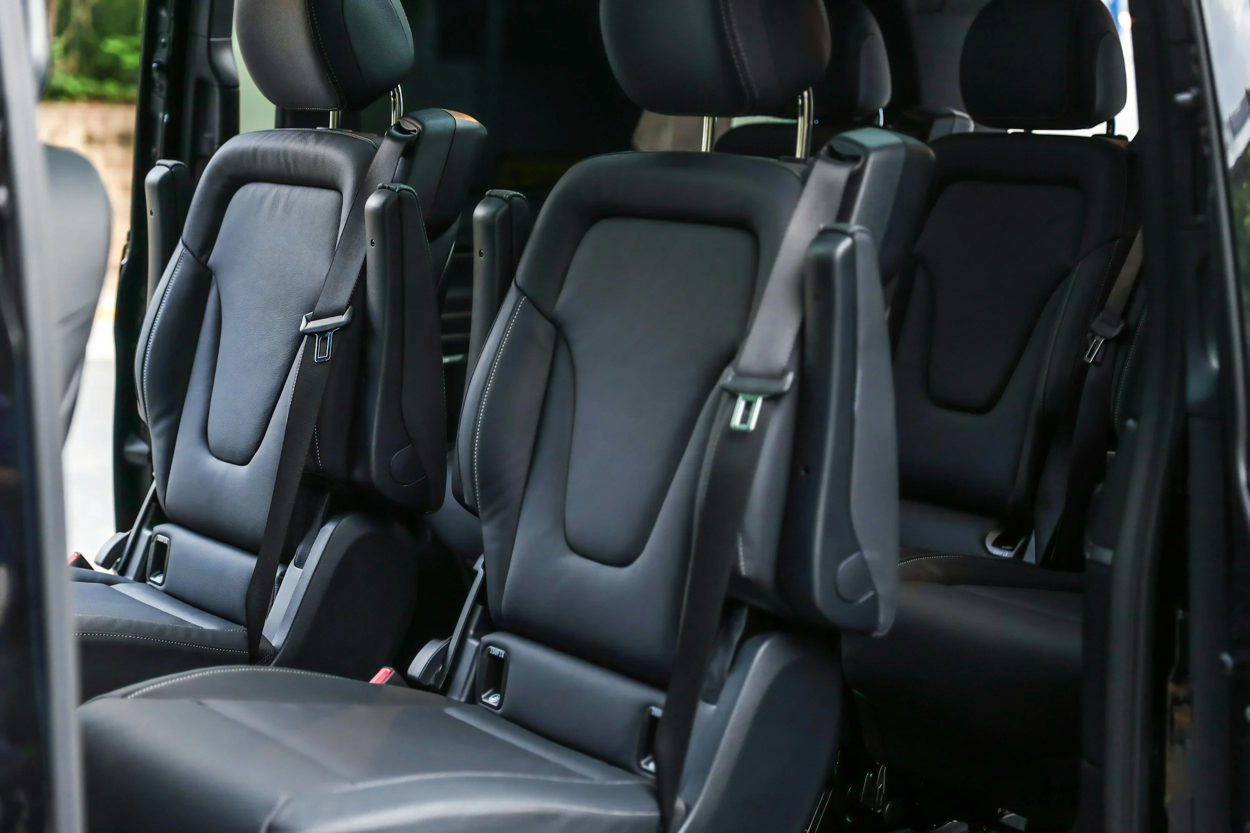 Interior of a black minivan showing three rows of black leather seats with headrests and seat belts.