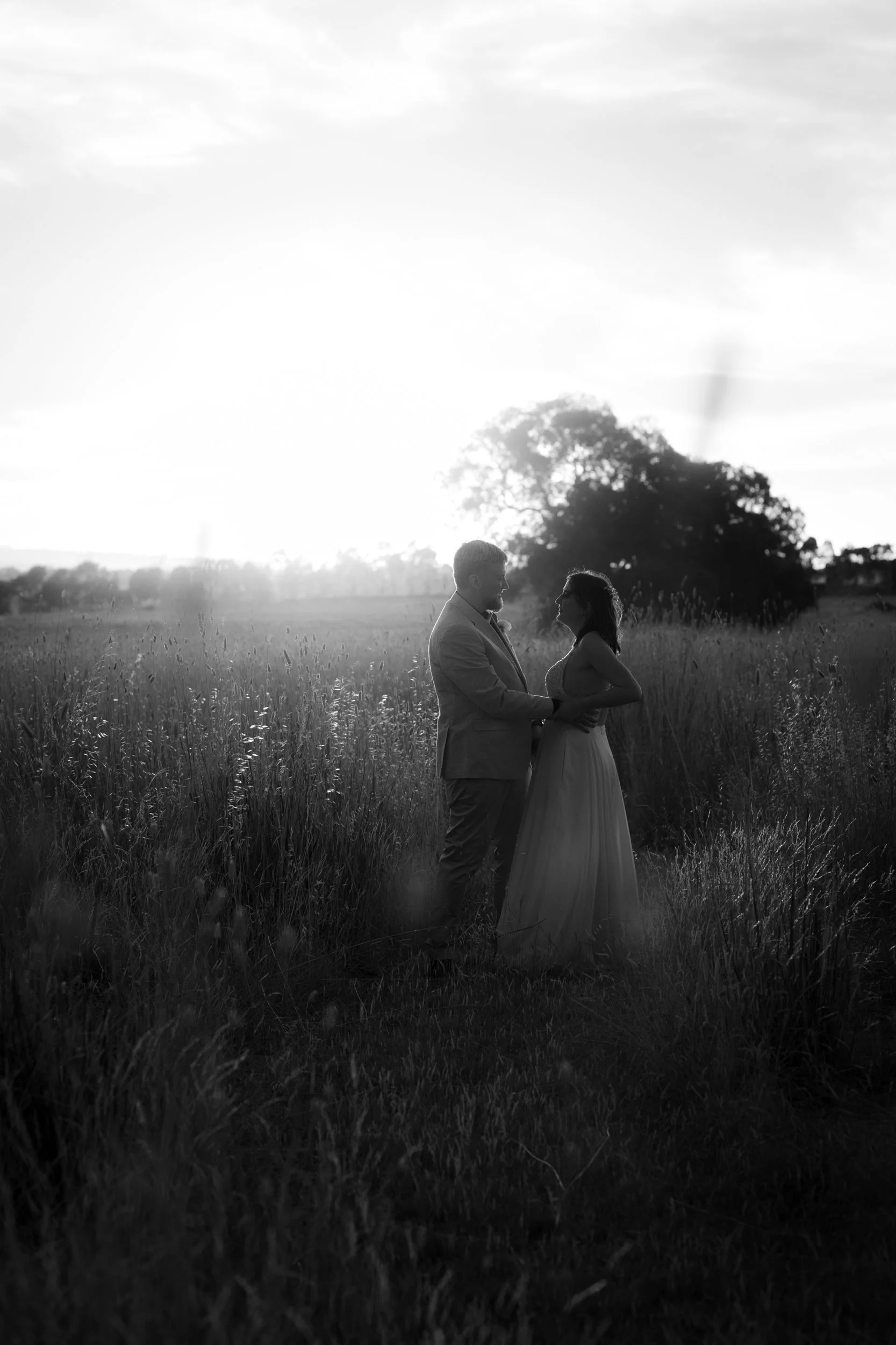 Long dining table set with white tablecloth, pink plates, silverware, and elegant pink and red floral centerpieces in black vases, surrounded by black chairs, in a dimly lit room.