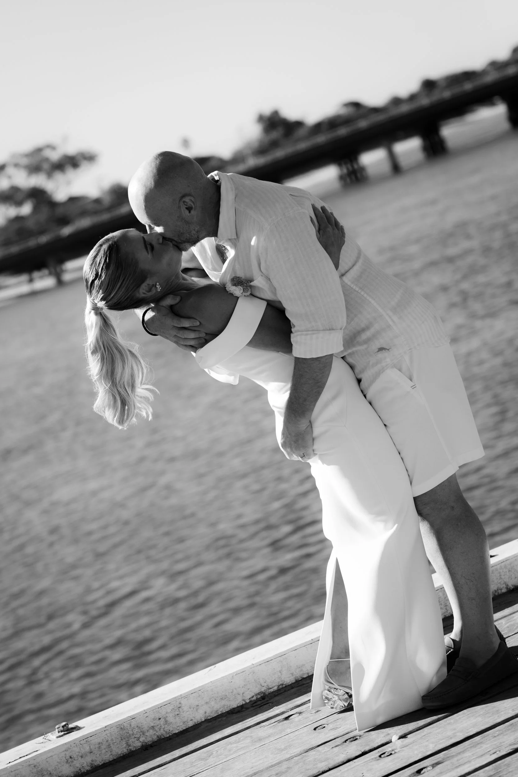 A floral arrangement with purple, pink, and white flowers, including delphiniums and orchids, with green leafy foliage, arranged on a white pedestal against a bright background.