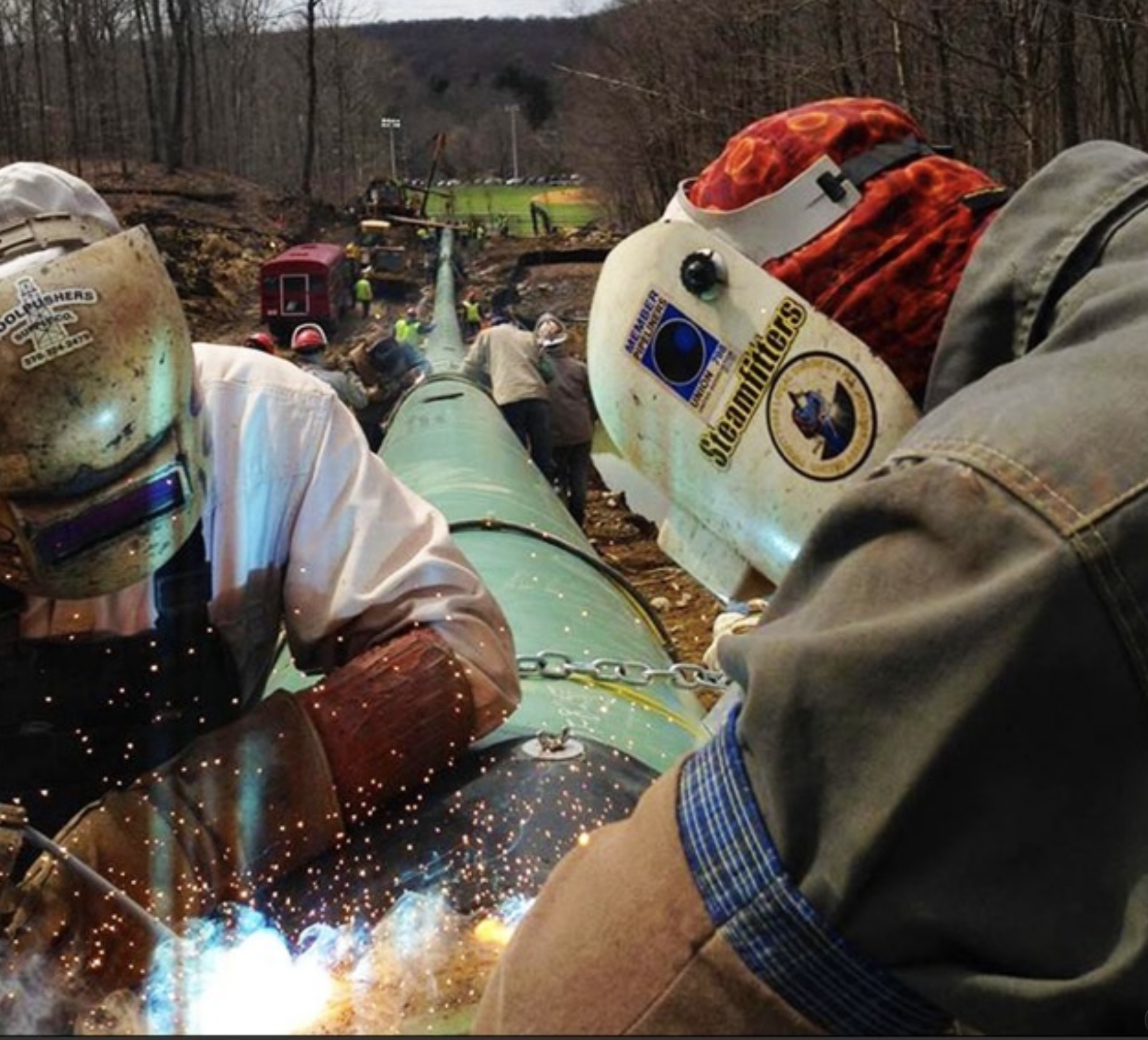 Pipeline construction welders wearing protective safety equipment while welding steel pipe at an oil and gas construction site.