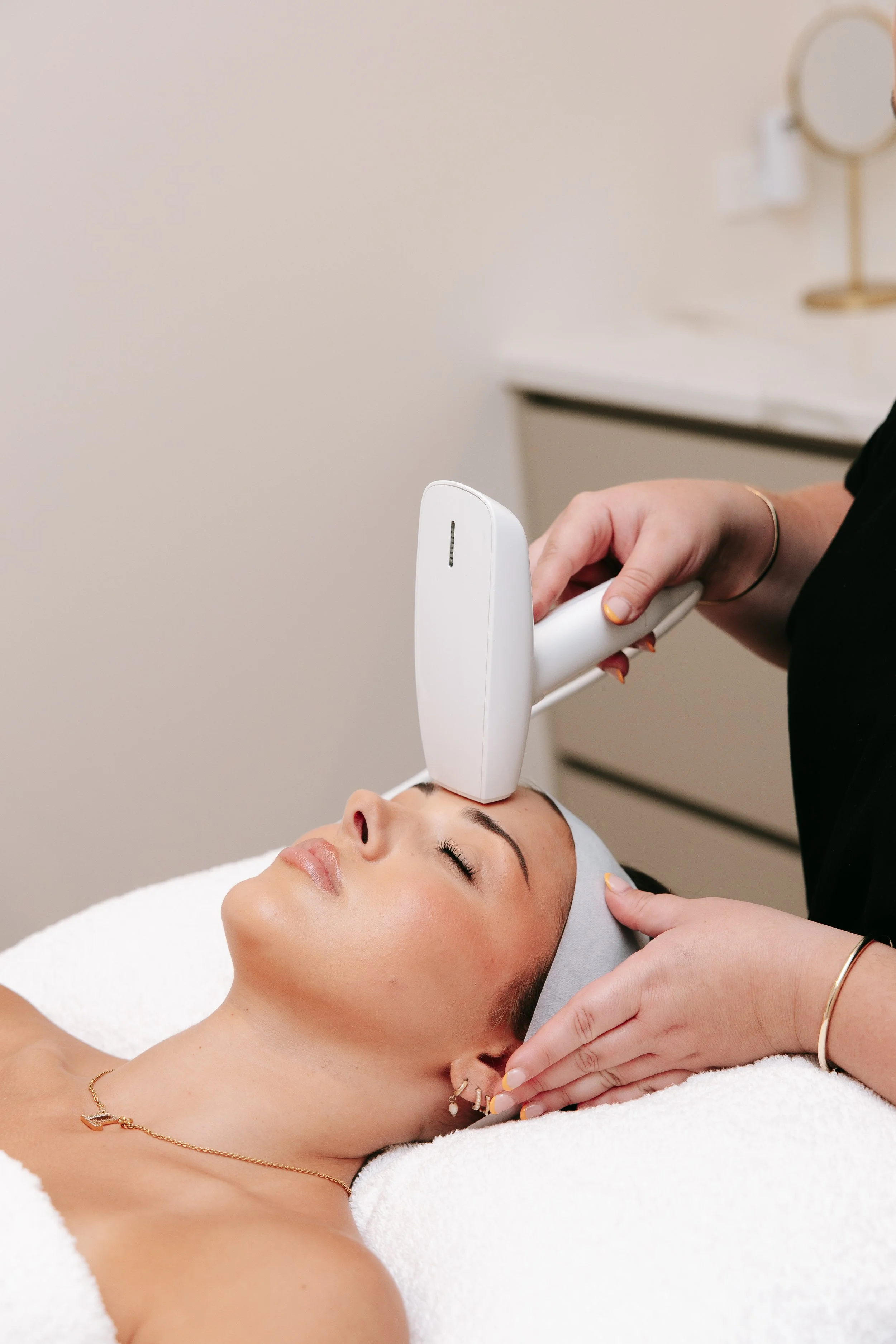 A woman receiving a facial treatment with a device on her forehead at a spa or clinic.