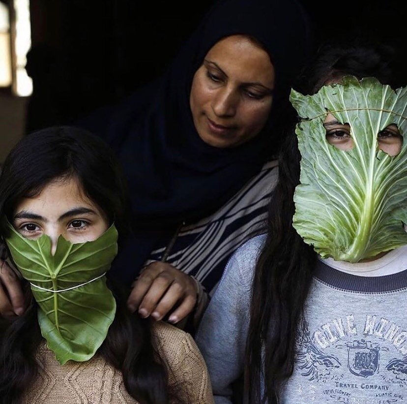 A Palestinian mother entertains her children with makeshift masks made of cabbage as she cooks