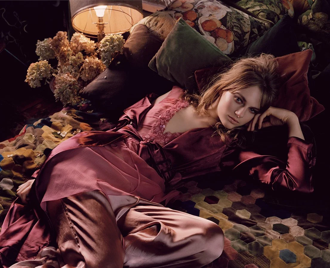 fashion editorial girl lying on patchwork bedspread and cushions wearing pink silk dress top and trousers