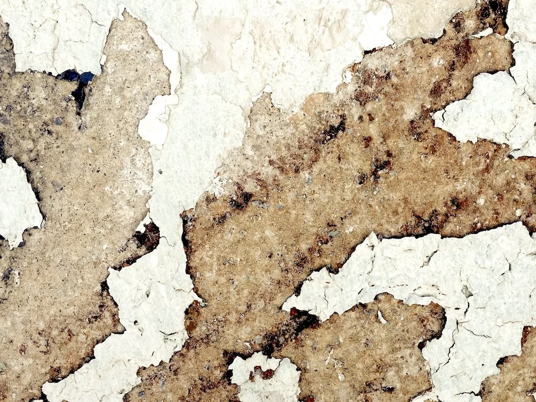 Close-up of peeling paint on a wall revealing rusted metal underneath.