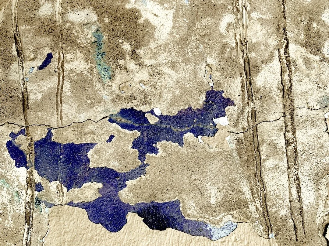 Close-up of a damaged tiled floor with cracked tiles and peeling paint, revealing dark blue underlayers.