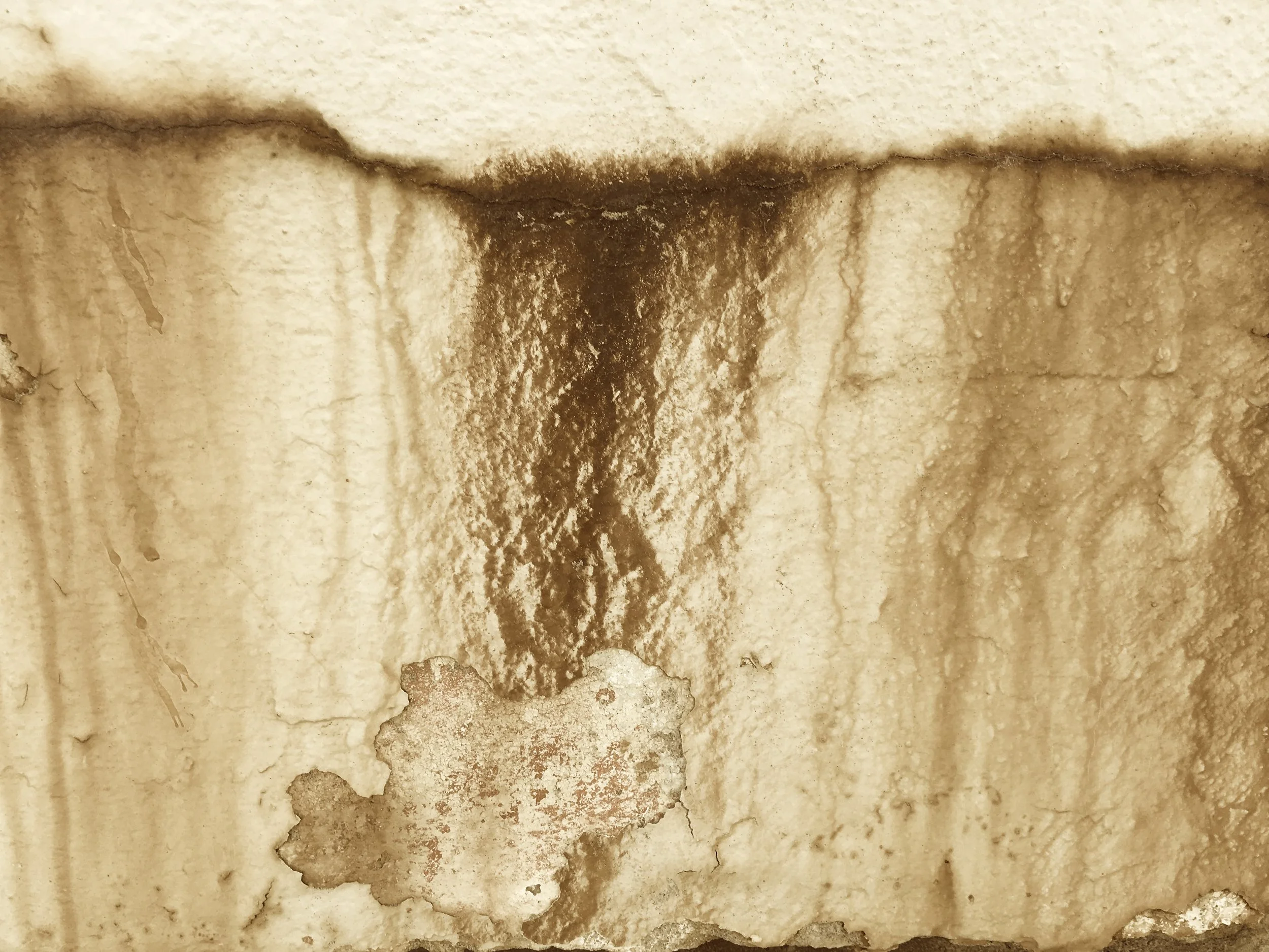 Close-up of a stained and weathered wooden surface, with a dark streak and peeling paint.