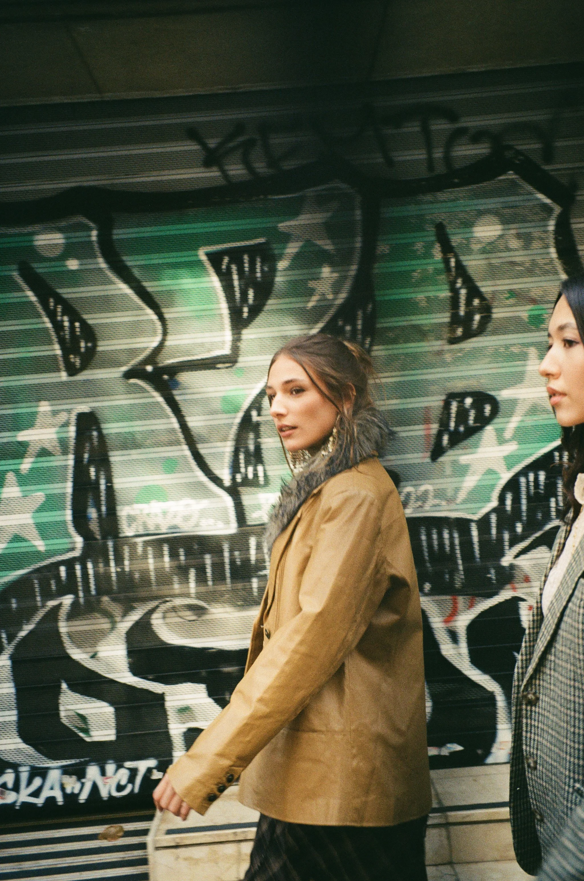 Two women walking past graffiti art on a wall in an urban setting.