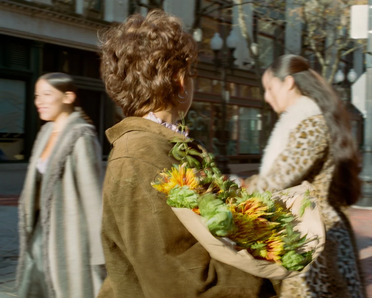 A woman holding a bouquet of flowers on a city street, with two other women walking by in the background.
