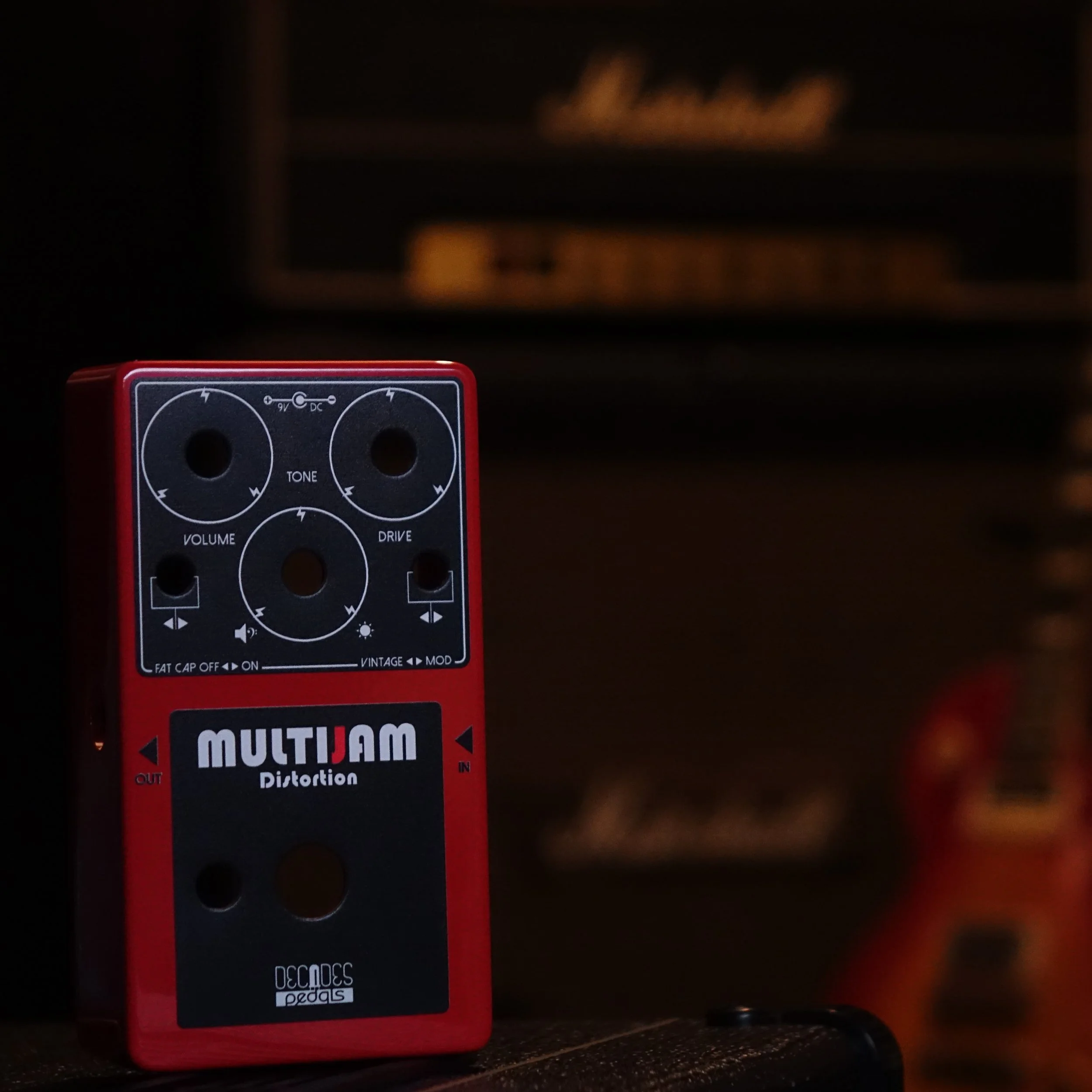 Close-up of a red guitar effects pedal labeled MULTIAM Distortion with various control knobs and switches.