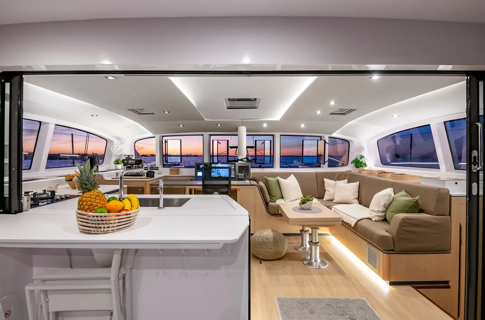 Interior of a yacht with a kitchen and a seating area, seen during sunset through large windows.