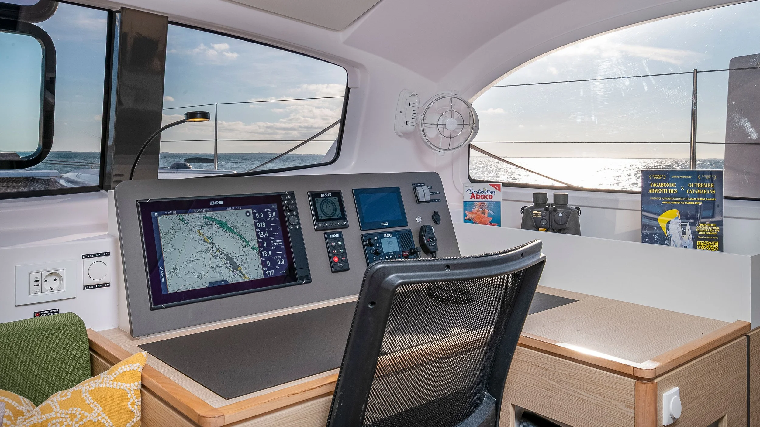 Navigation and communication equipment console on a boat with a view of the water and sky through windows.