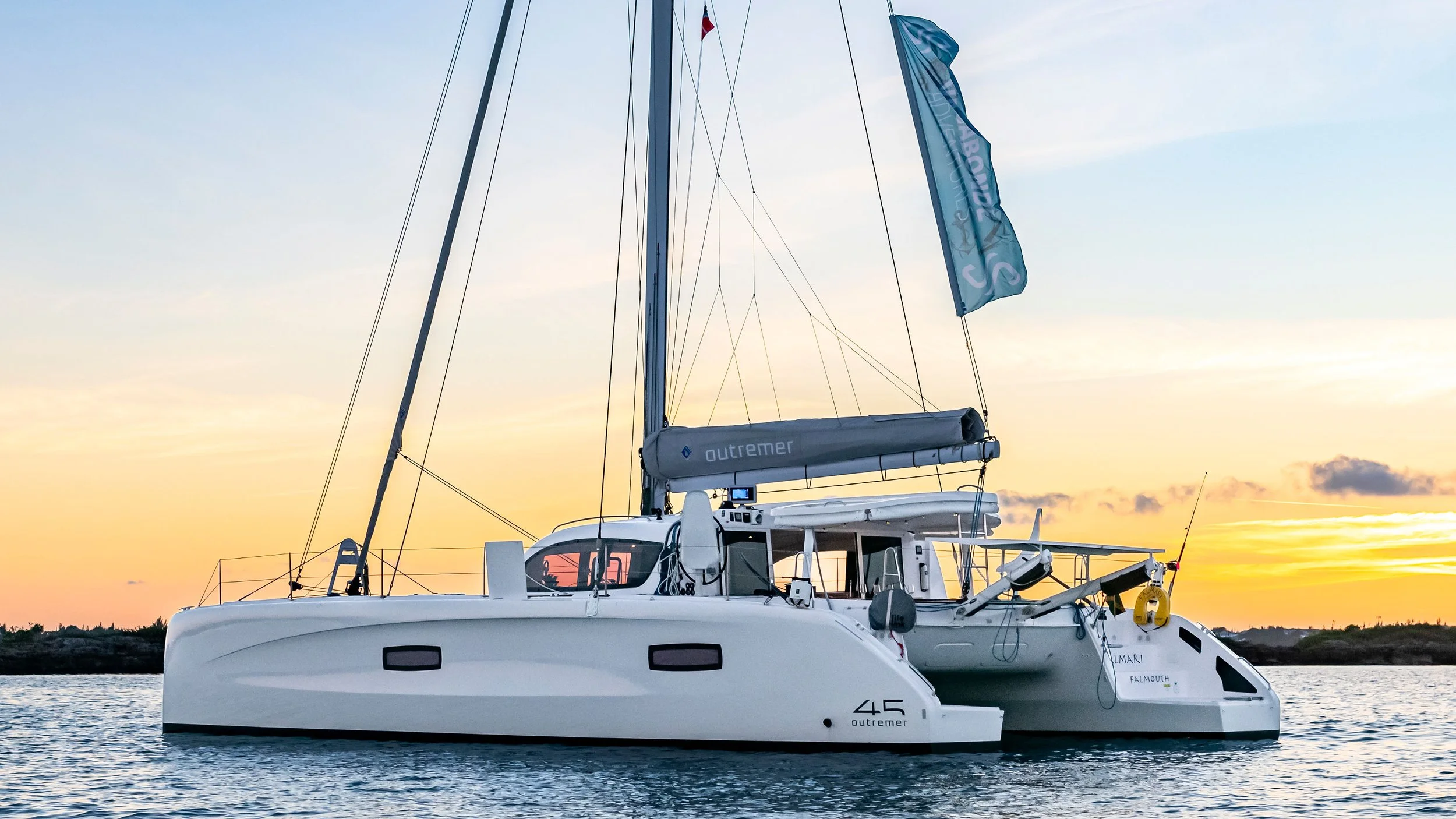 A white Outremer 45 sailing catamaran on calm water at sunset with a yellow and orange sky.