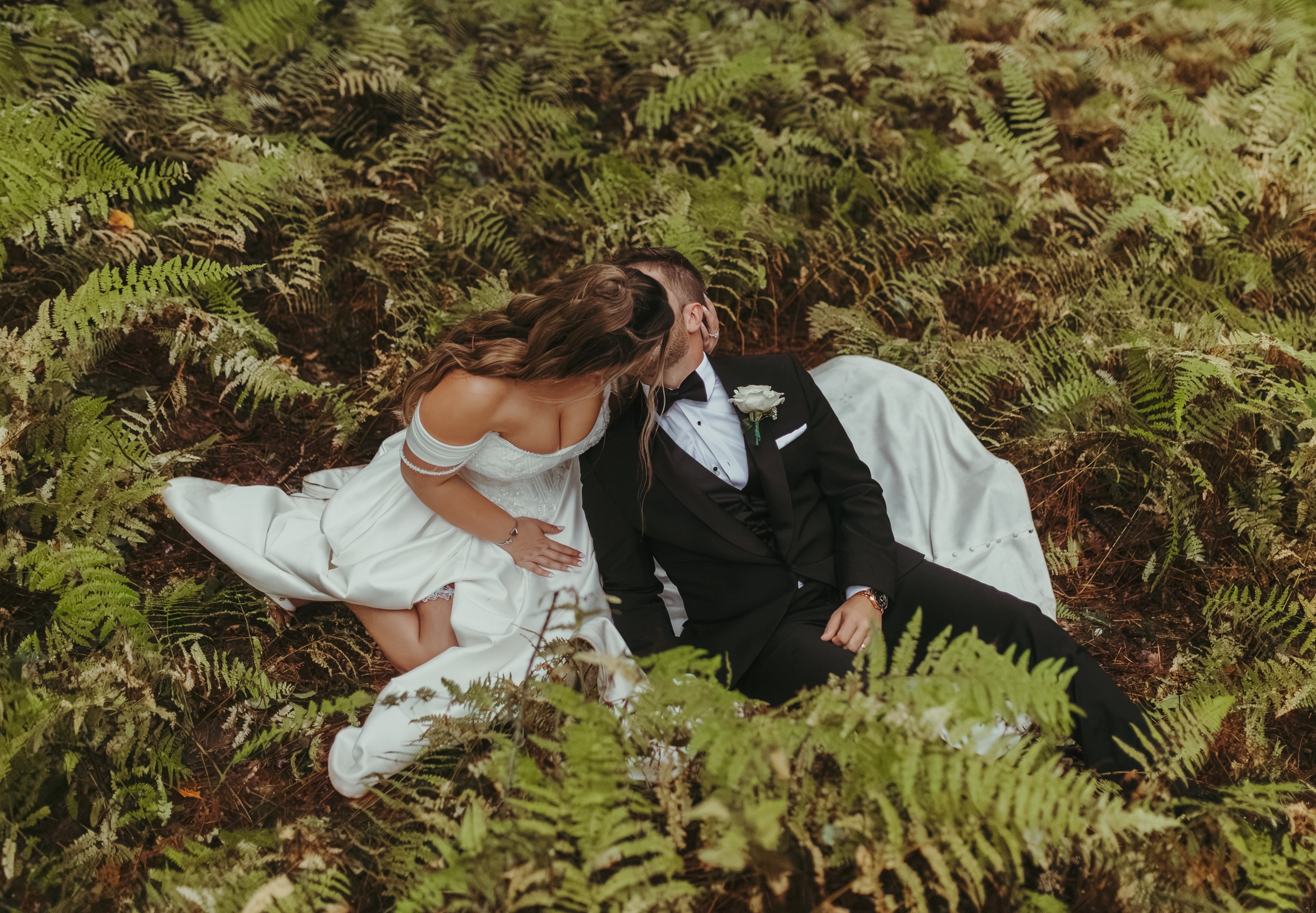 A bride and groom sit in ferns