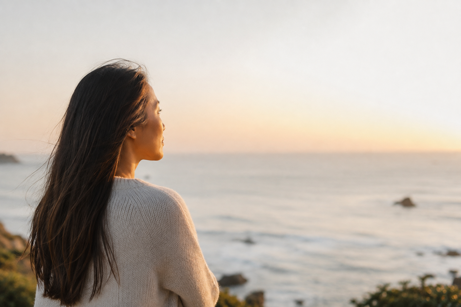 A woman with long dark hair looking out over the ocean during sunset
