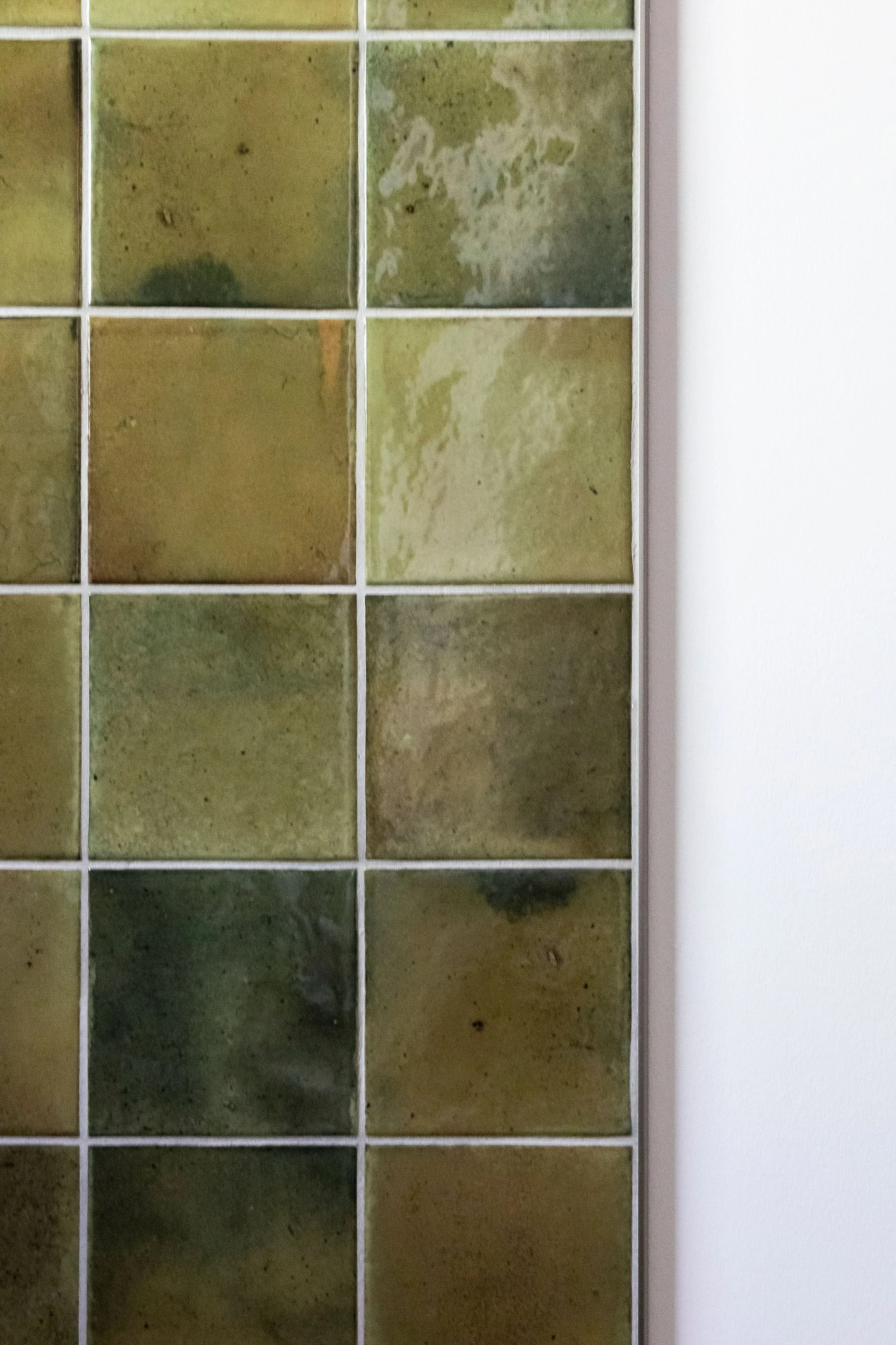 A close-up of a grid of glass blocks with various shades of green and a white frame.