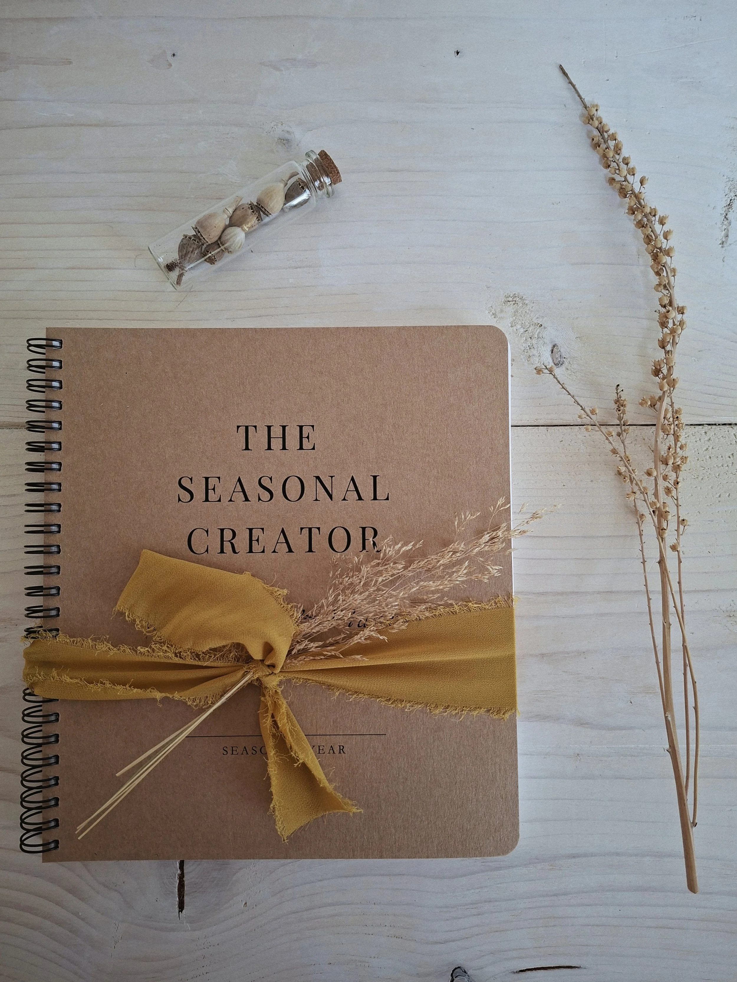 The Seasonal Creator Workbook & Planner wrapped with ochre ribbon and dried grasses.