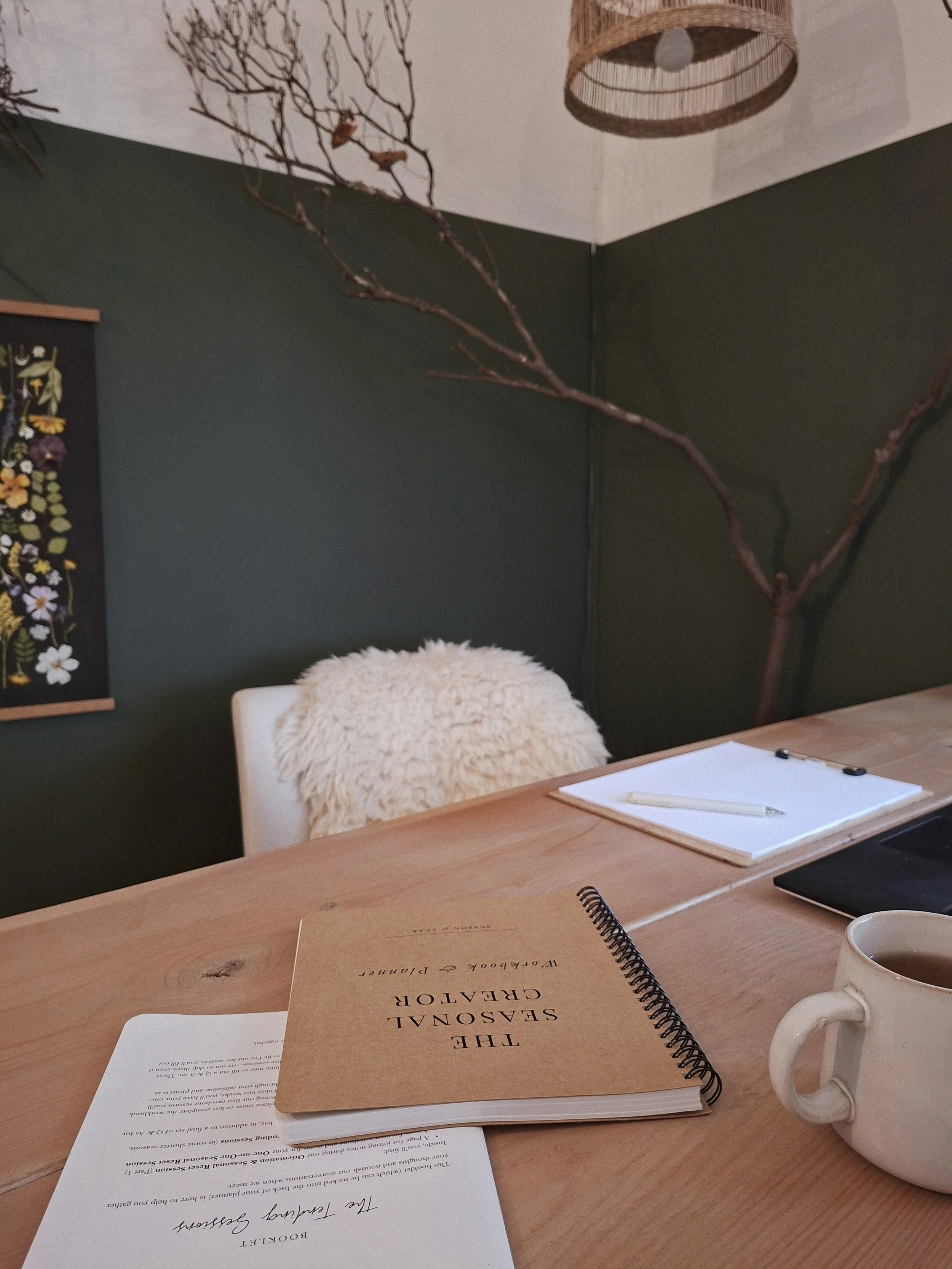 The Seasonal Creator Workbook & Planner on a pale wood table with session materials, notebook, laptop, and mug.