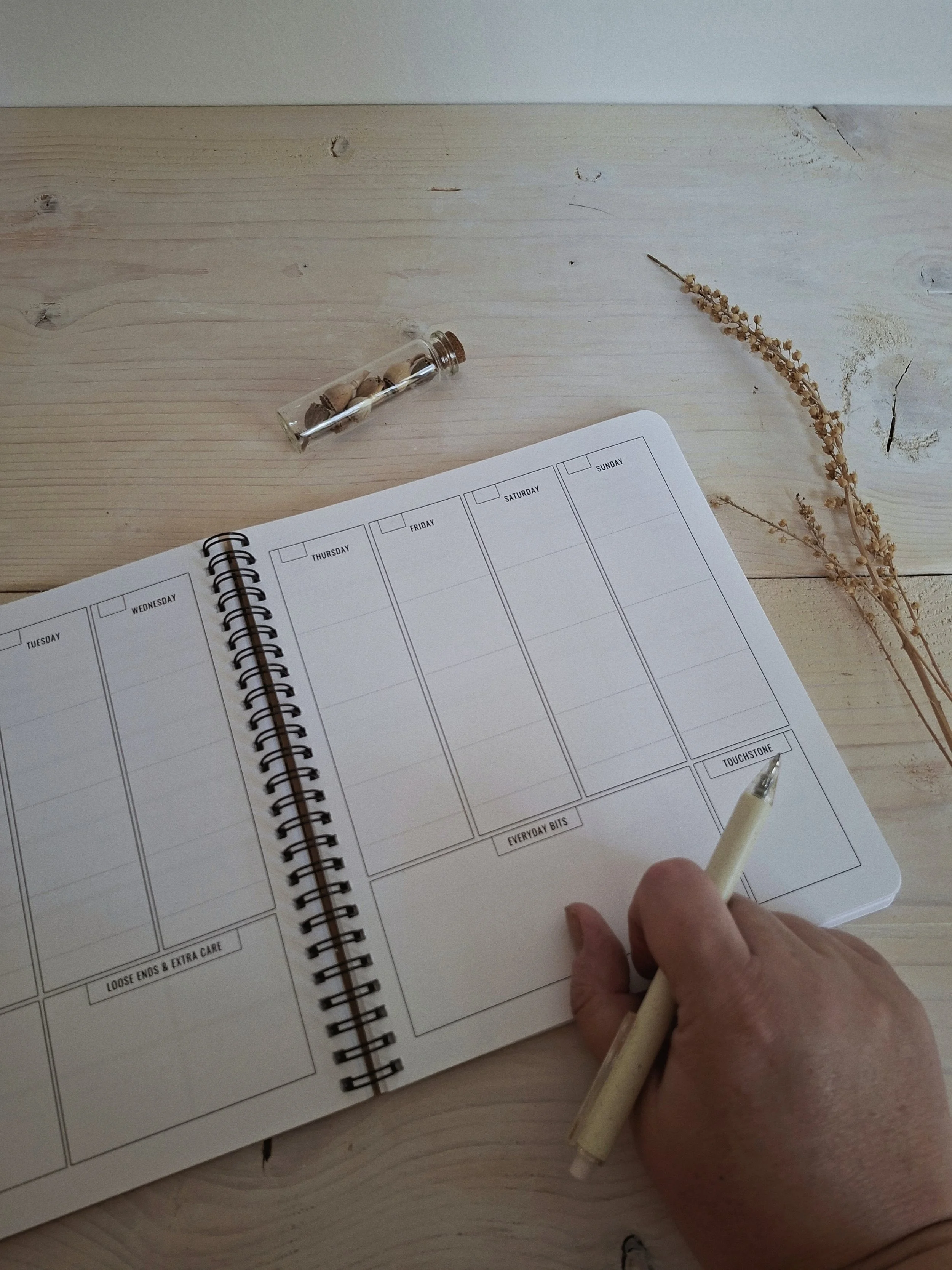 The Seasonal Creator Workbook & Planner open to a weekly planning spread, with a hand holding a pen.