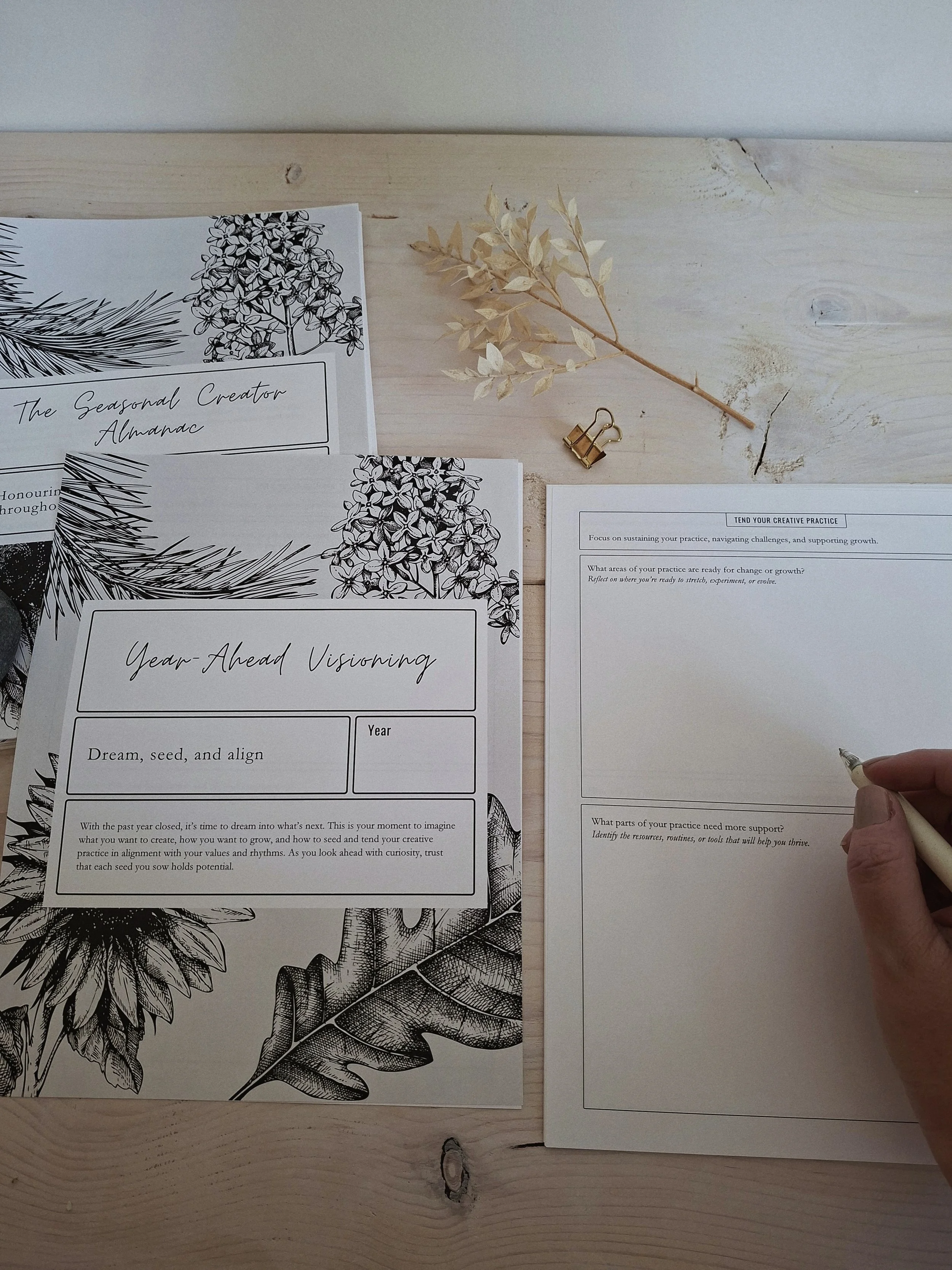 The Seasonal Creator Almanac open to the Year-Ahead Visioning Workbook, alongside a page being completed by hand.