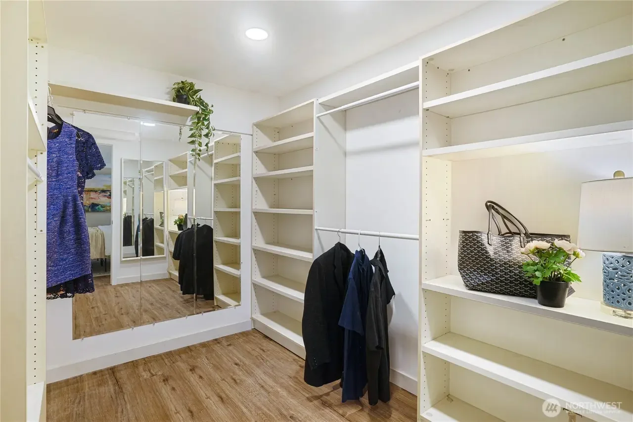 Empty walk-in closet with white shelving, a hanging rod with clothes, a mirror, and decorative items on shelves.