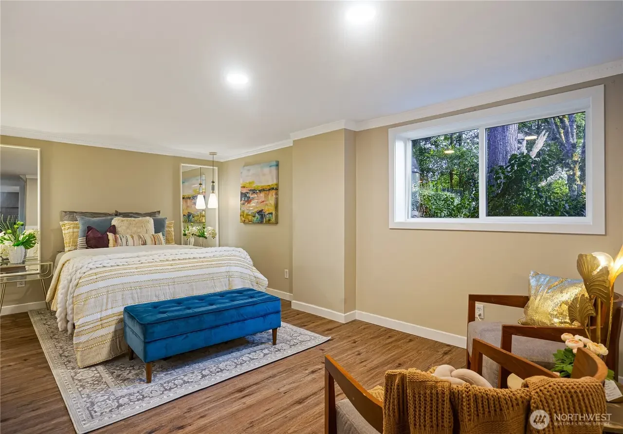 Bedroom with bed, blue bench, window overlooking trees, chairs, and wall art.