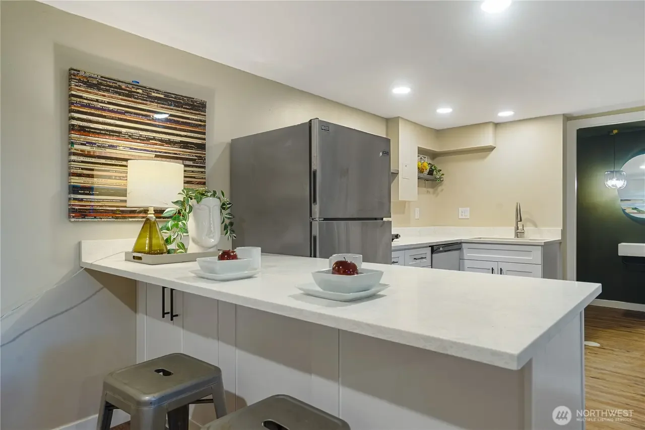 Kitchen with white countertops, stainless steel refrigerator, white cabinets, and a black wall with a round mirror.