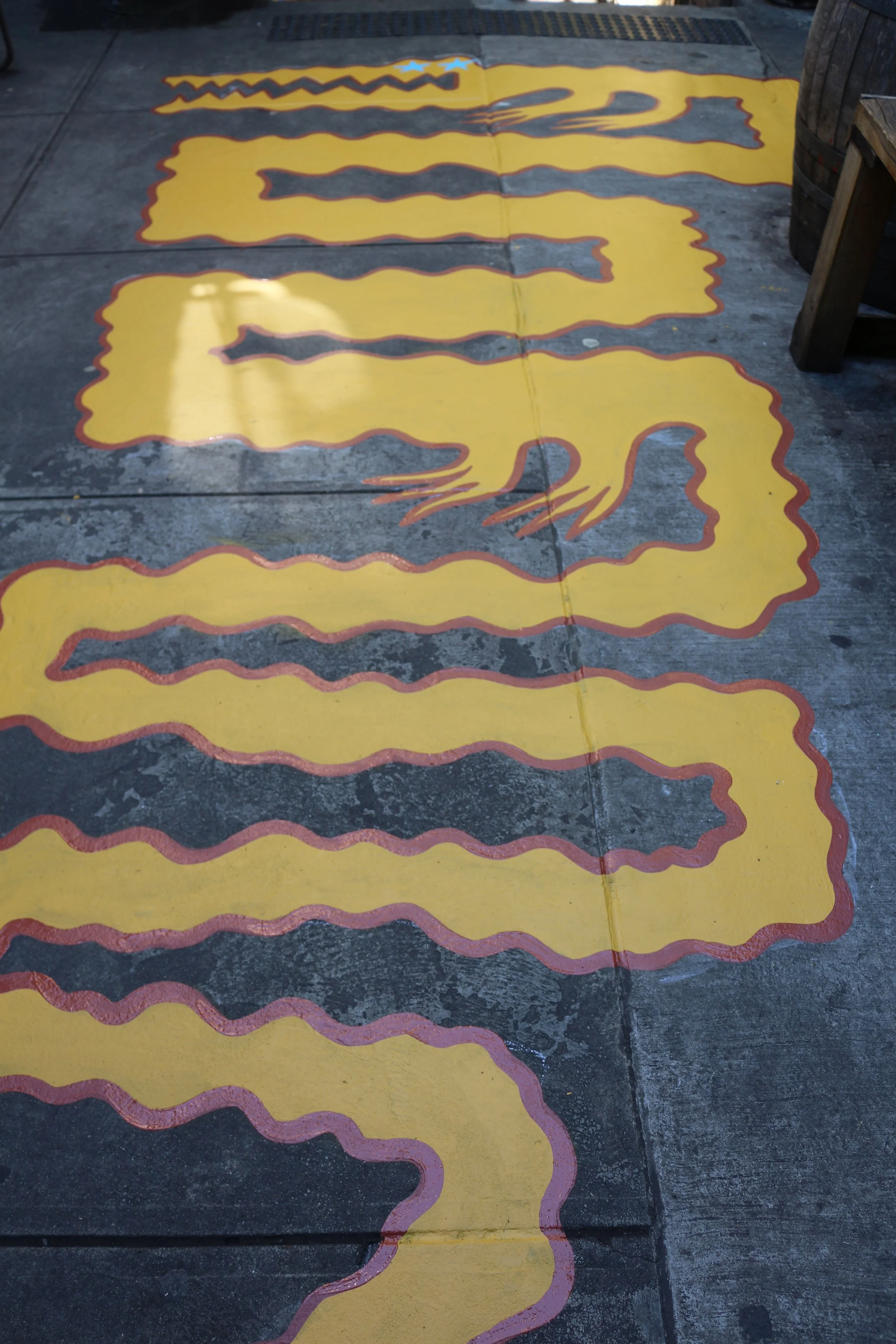A floor mural of a giant yellow crocodile painted on the concrete floor of a beer garden.