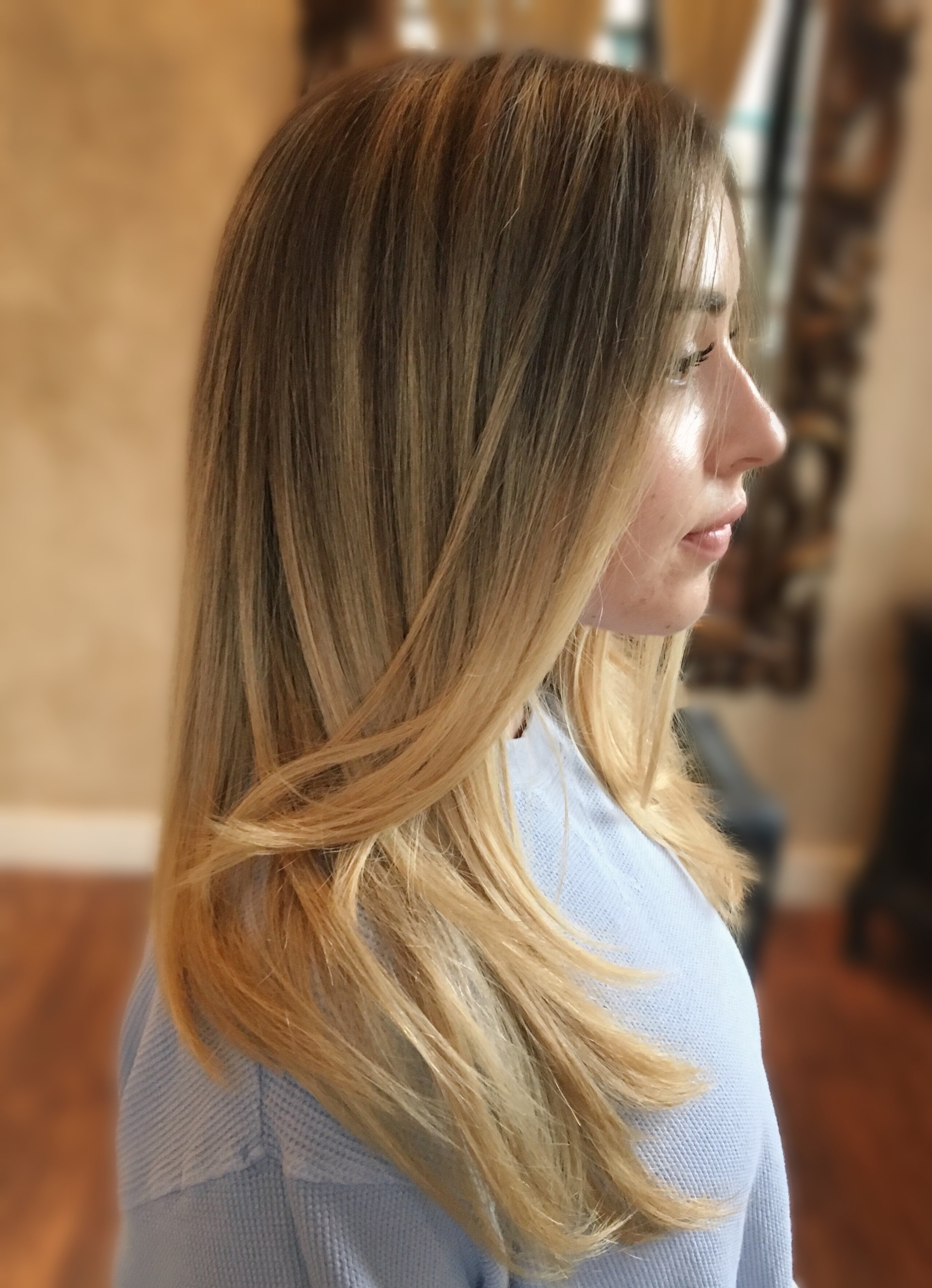 Profile view of a woman with long, straight blond hair wearing a light blue sweater.