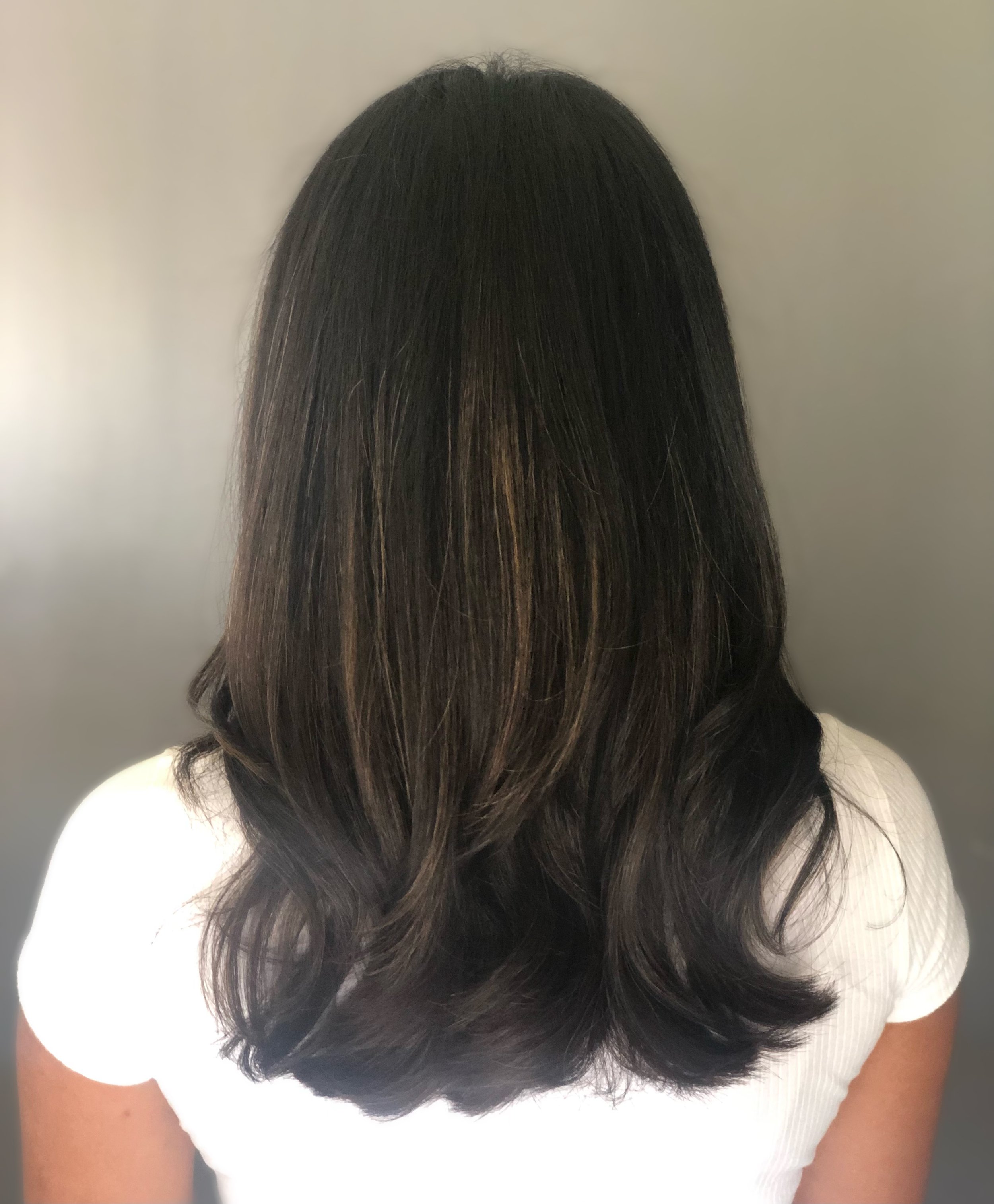 Woman with long dark hair and white top, back view.
