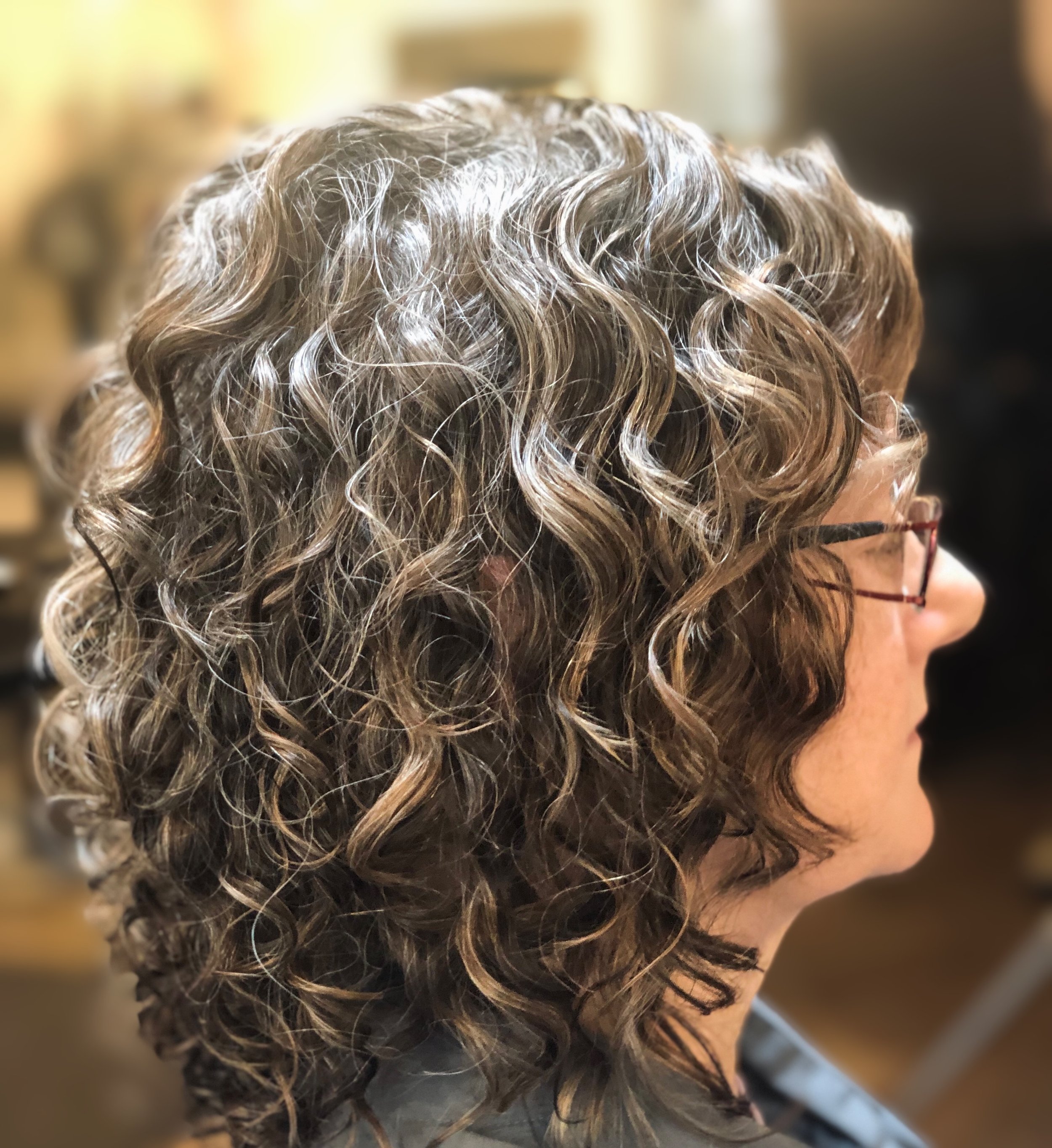 Woman with curly brown hair wearing glasses, viewed from the side.