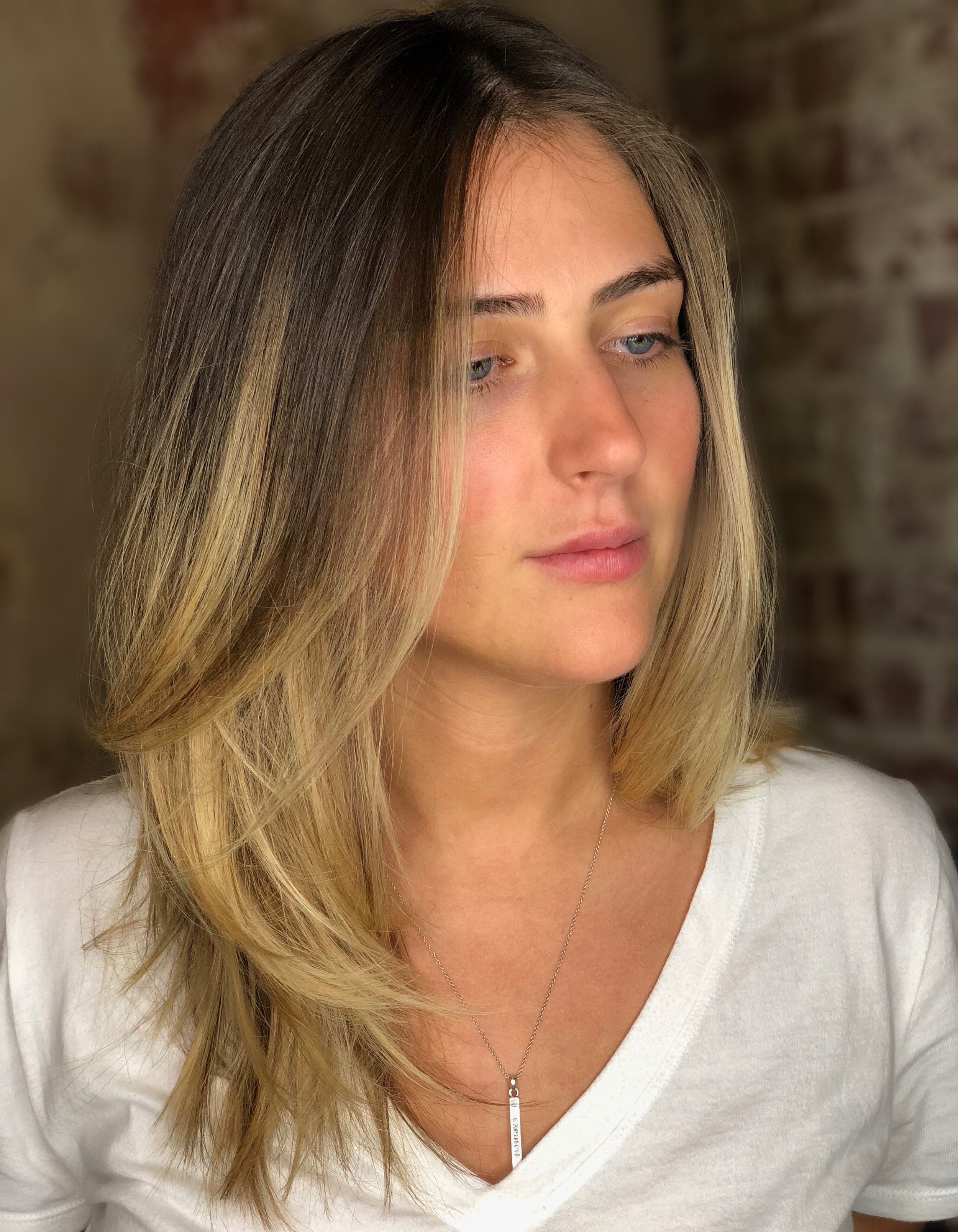 Woman with long blonde hair wearing a white V-neck shirt and necklace.