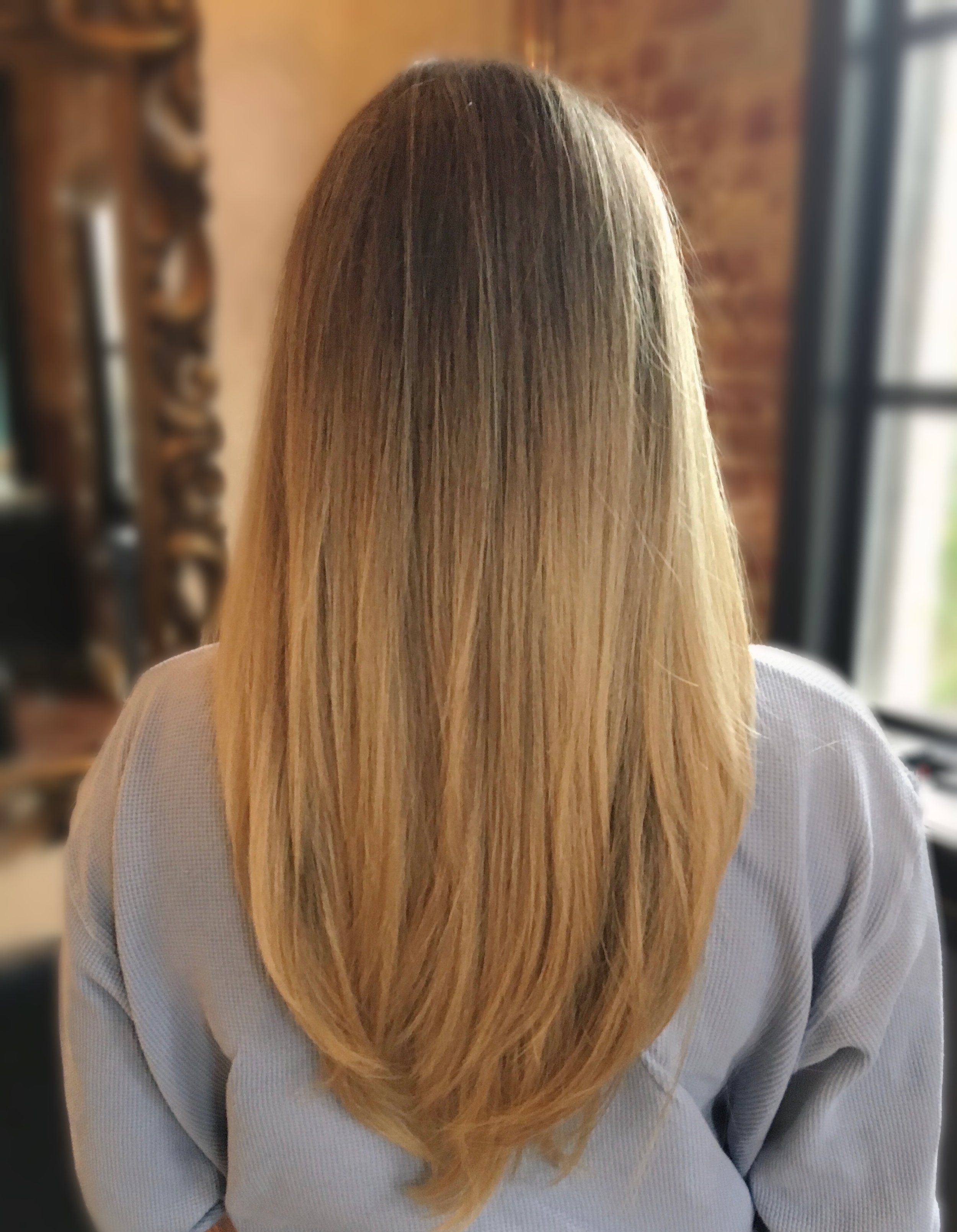 Long straight blonde hair from the back, indoors with a blurred background.