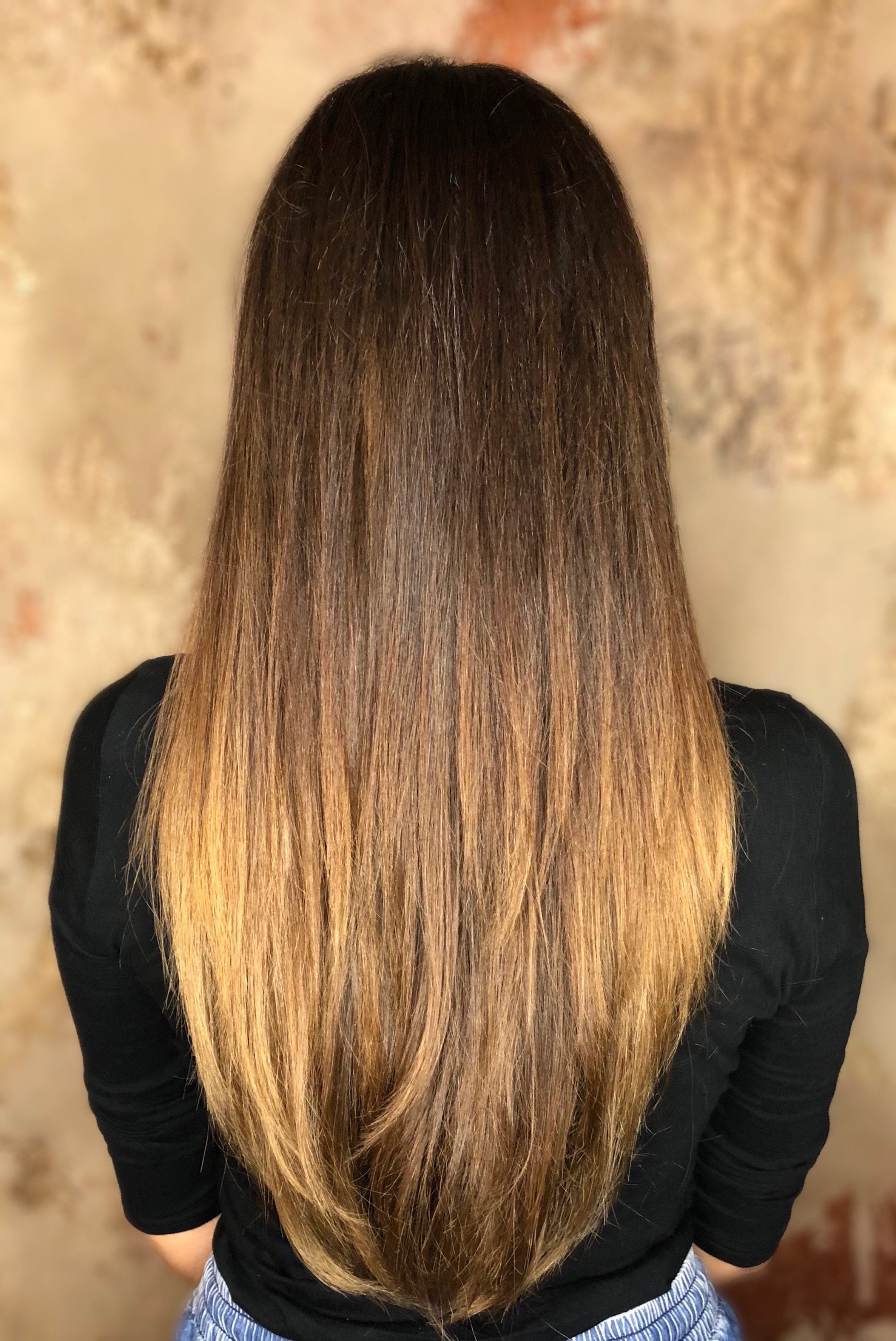 Woman with long straight brown hair in a black top, back view.
