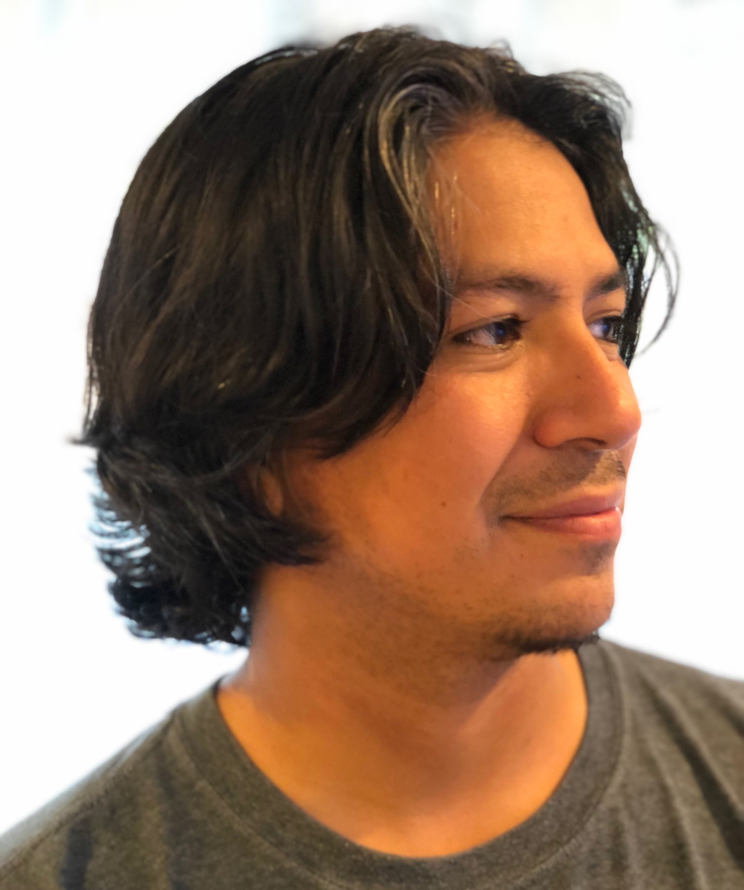 Close-up of a man with medium-length dark hair looking to the side, wearing a gray shirt.