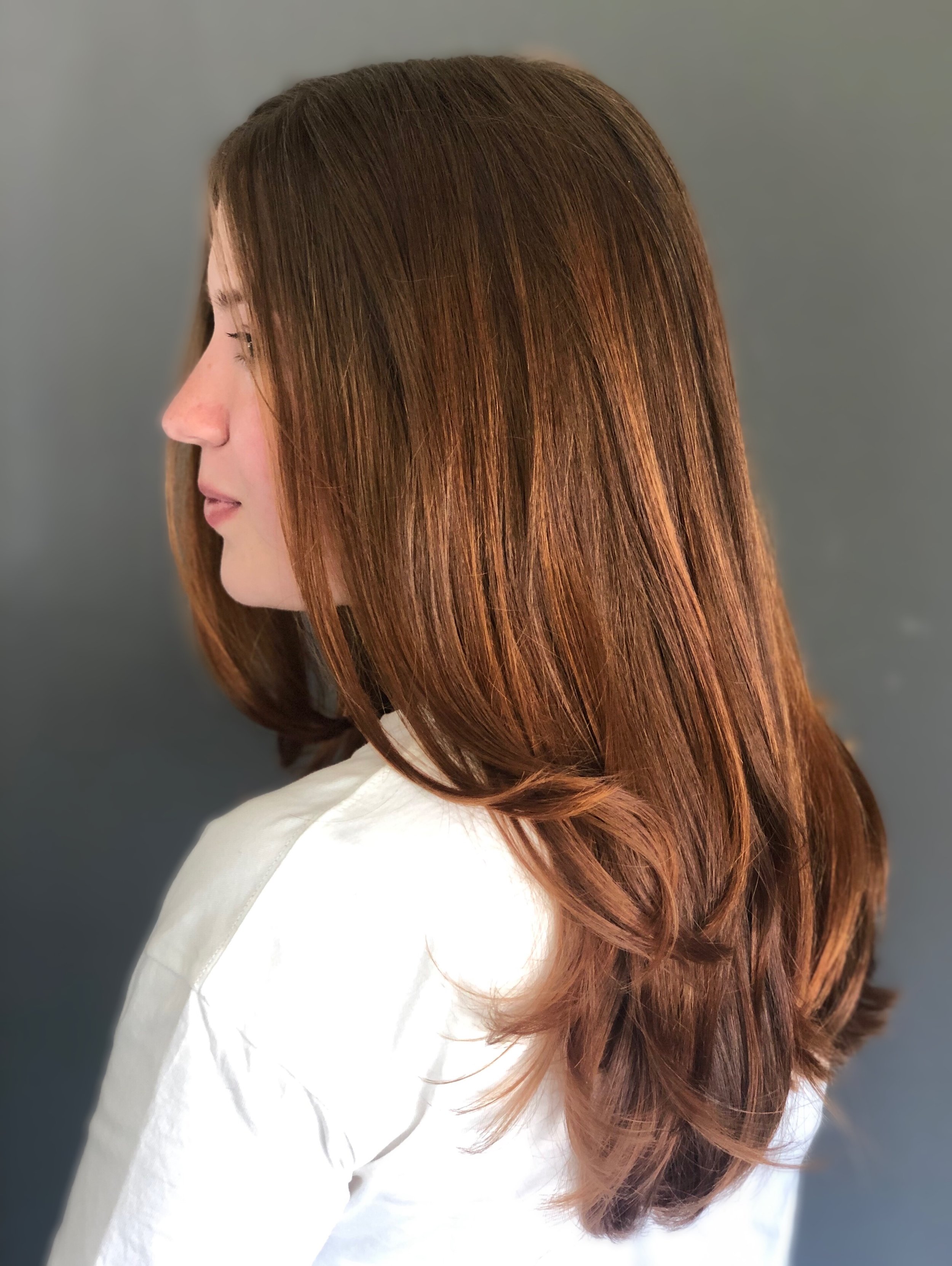 Profile view of a person with long, straight brown hair against a gray background.